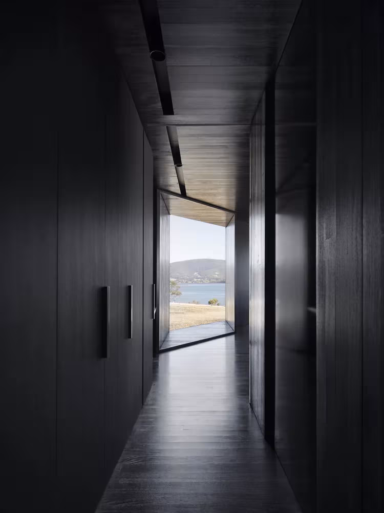 Pasillo oscuro con armarios negros que termina en una ventana al estuario en D'Entrecasteaux House