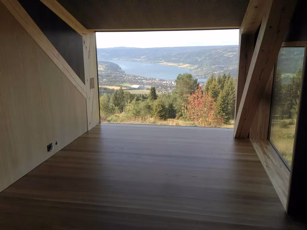 Estancia de madera con un gran hueco enmarcado que se abre al lago y al valle en la Villa Gudbrand