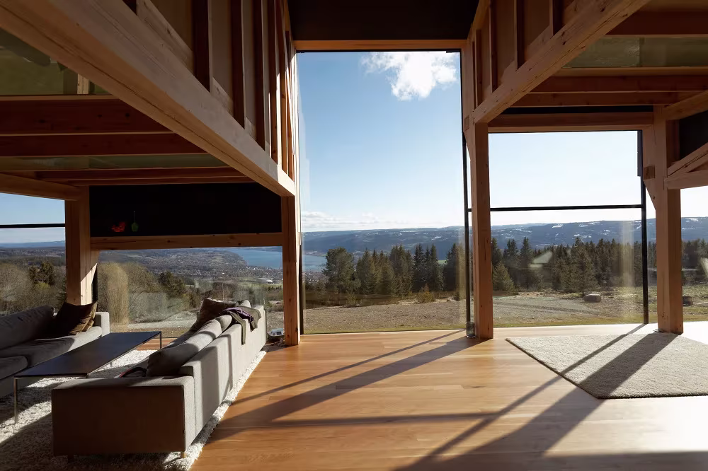 Salón a doble altura con sofá y gran ventanal con vistas al valle en la Villa Gudbrand, cerca de Lillehammer