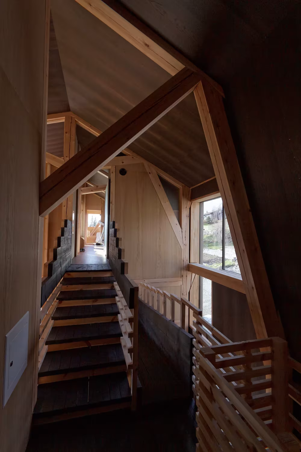 Pasillo con escalera y barandilla de listones bajo la estructura de madera inclinada de la Villa Gudbrand