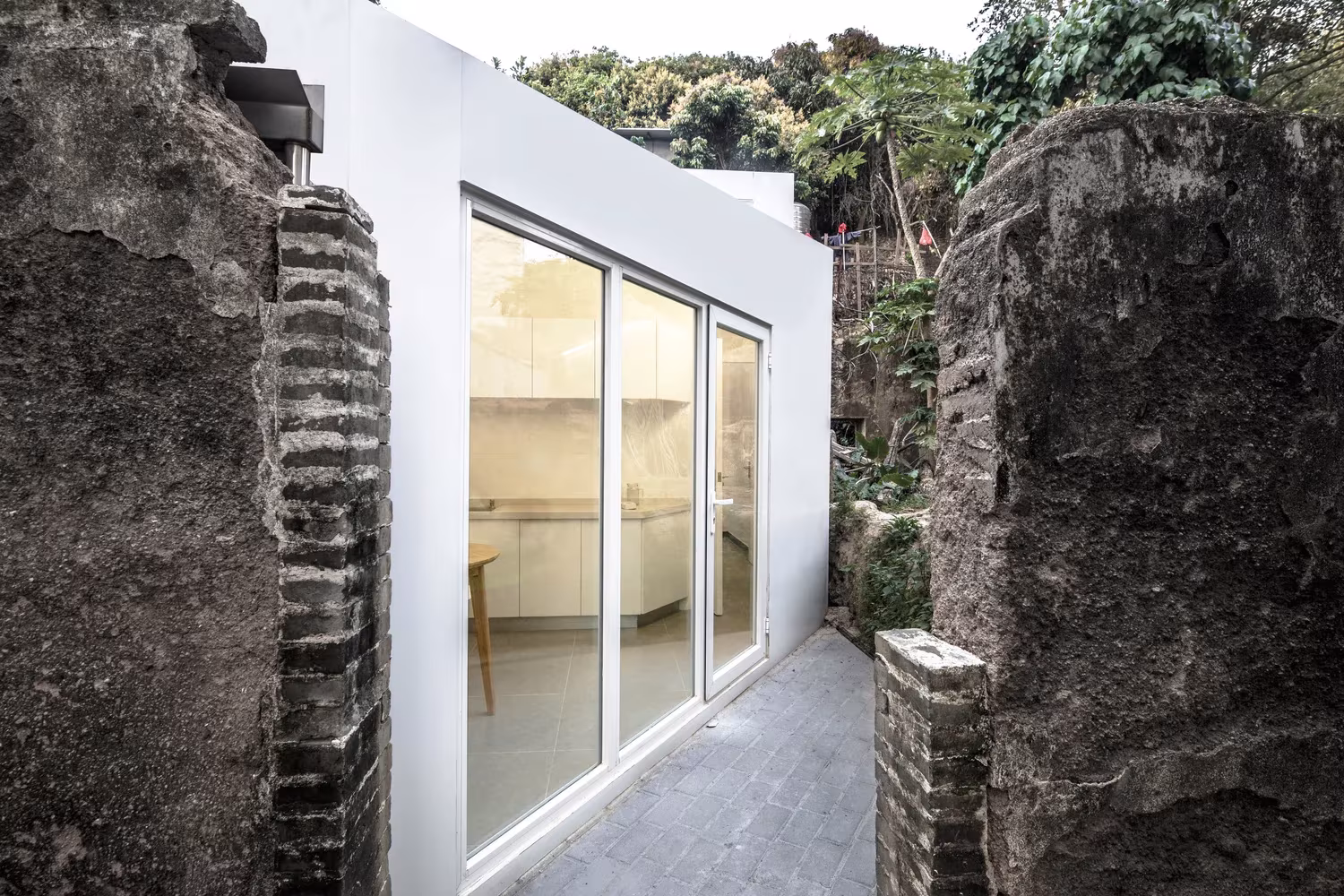 Fachada acristalada de la Plugin House entre dos muros de ladrillo antiguos en Shangwei, de PAO