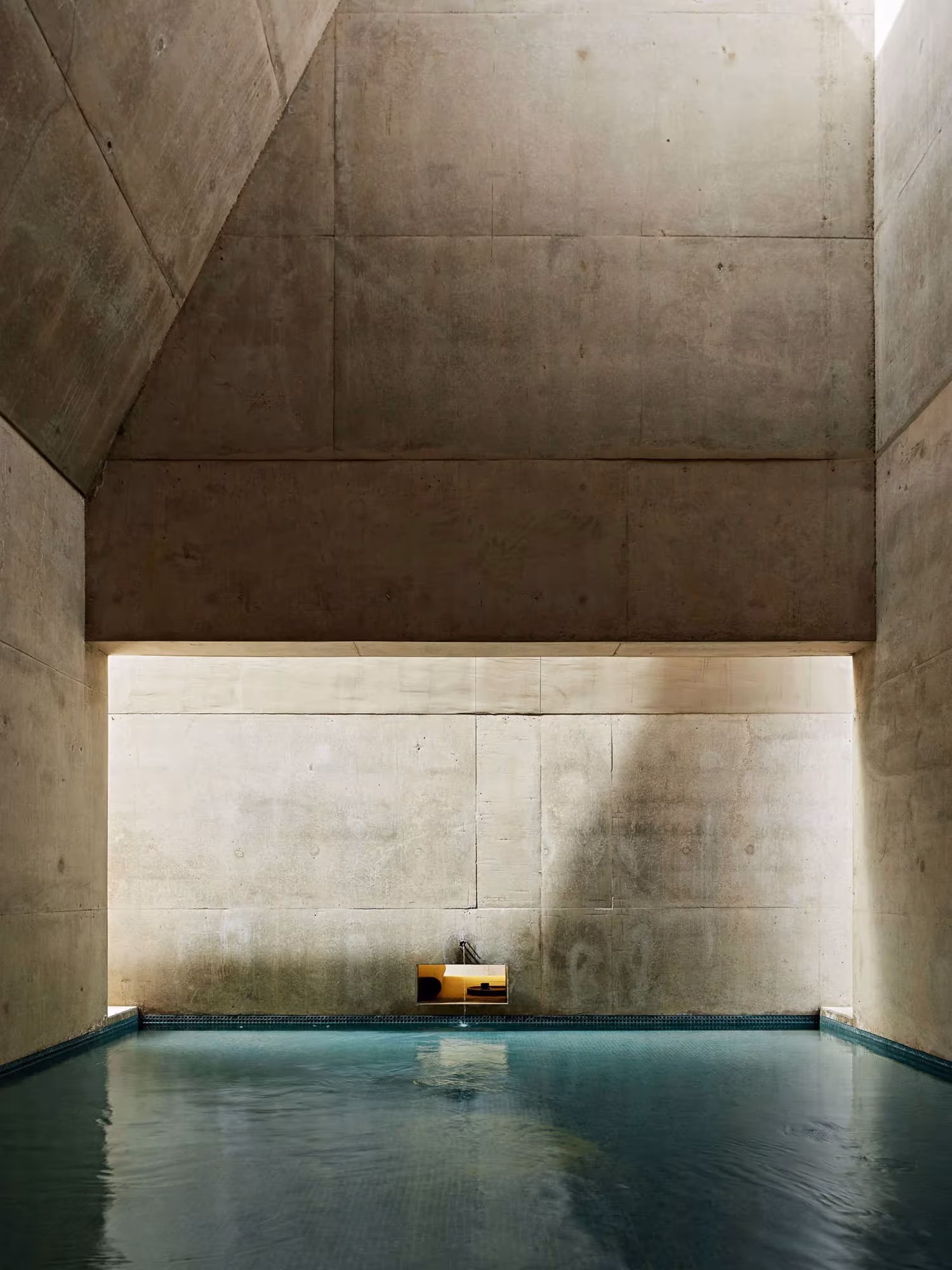 Piscina interior del Amangiri bajo un hueco de hormigón visto con luz cenital y pared rugosa