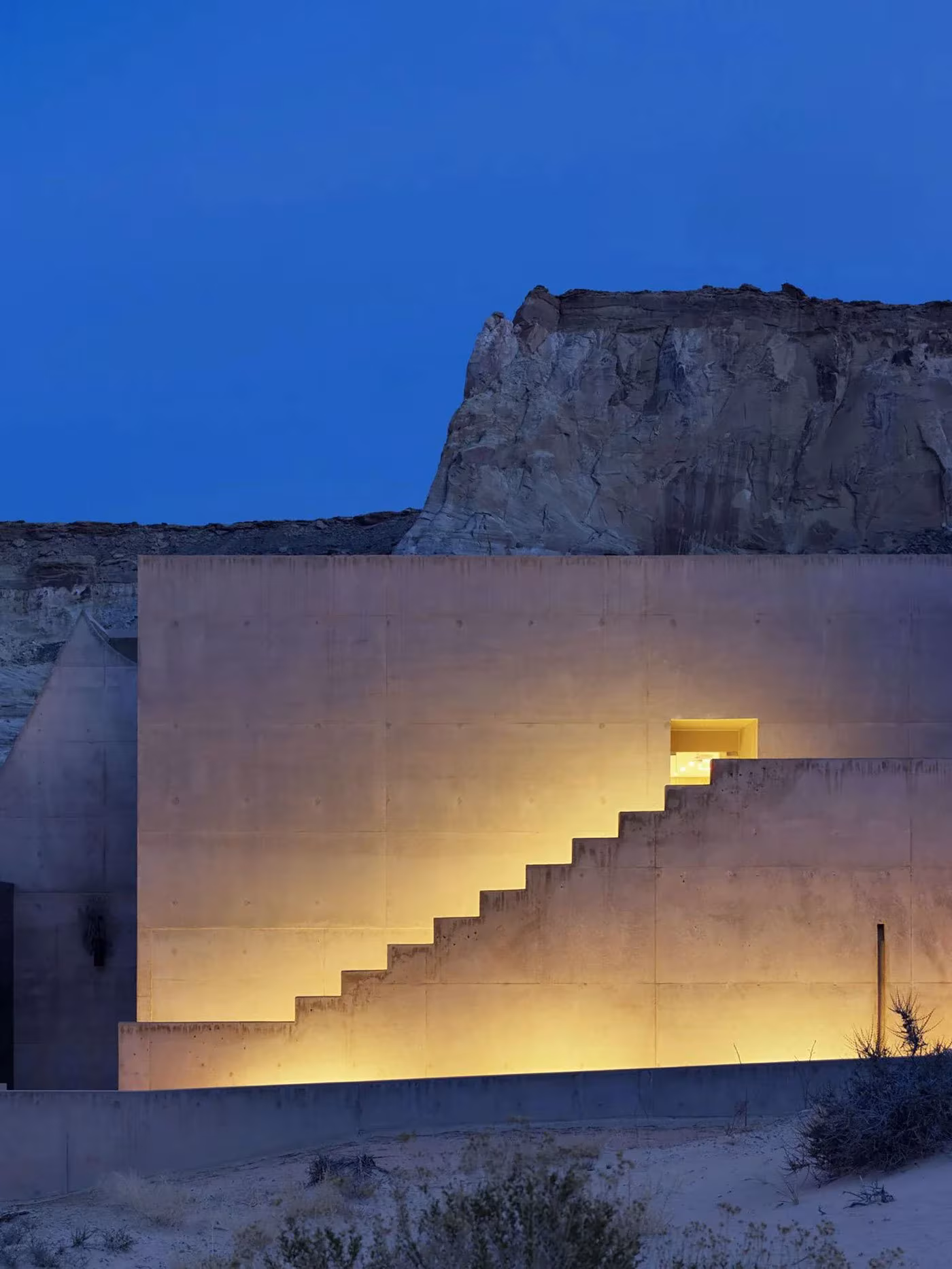 Escalera iluminada sobre un volumen de hormigón del Amangiri al anochecer, con la meseta de fondo