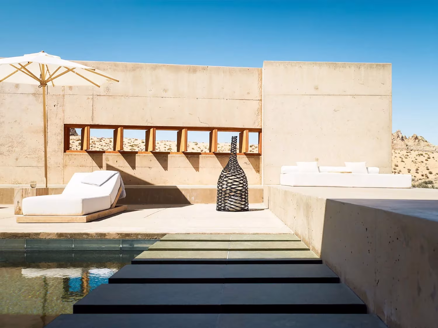 Terraza con tumbonas y pasos de piedra sobre la piscina del Amangiri, junto a un muro con hornacinas