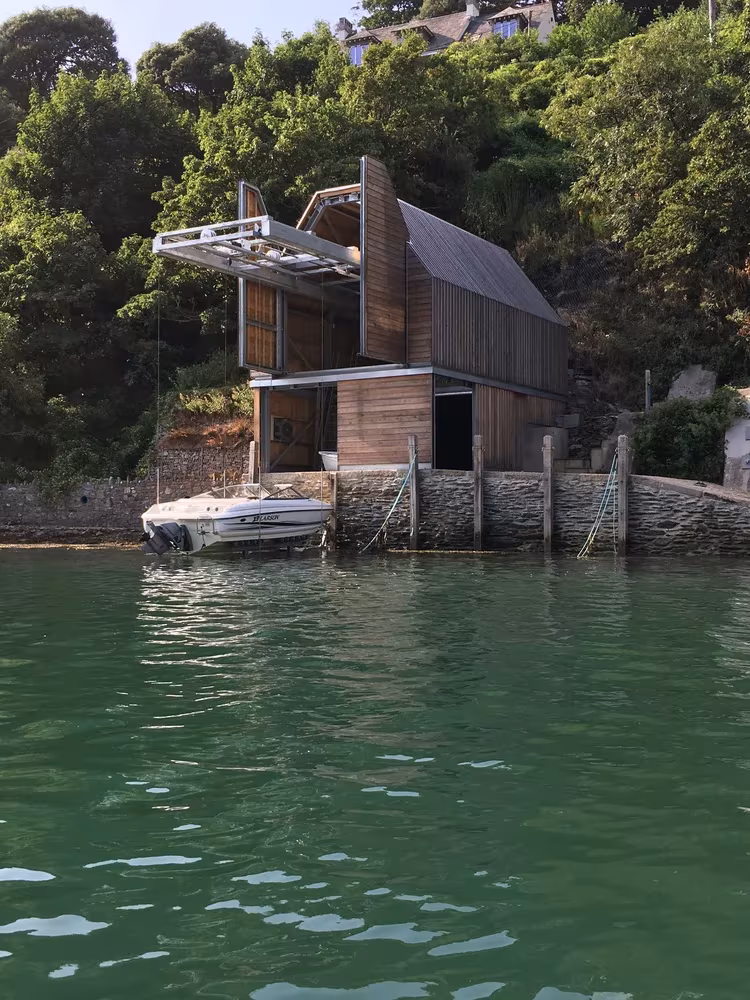 Berberis Boathouse con su cubierta de madera sobre el muro de piedra junto al agua verde del río Yealm