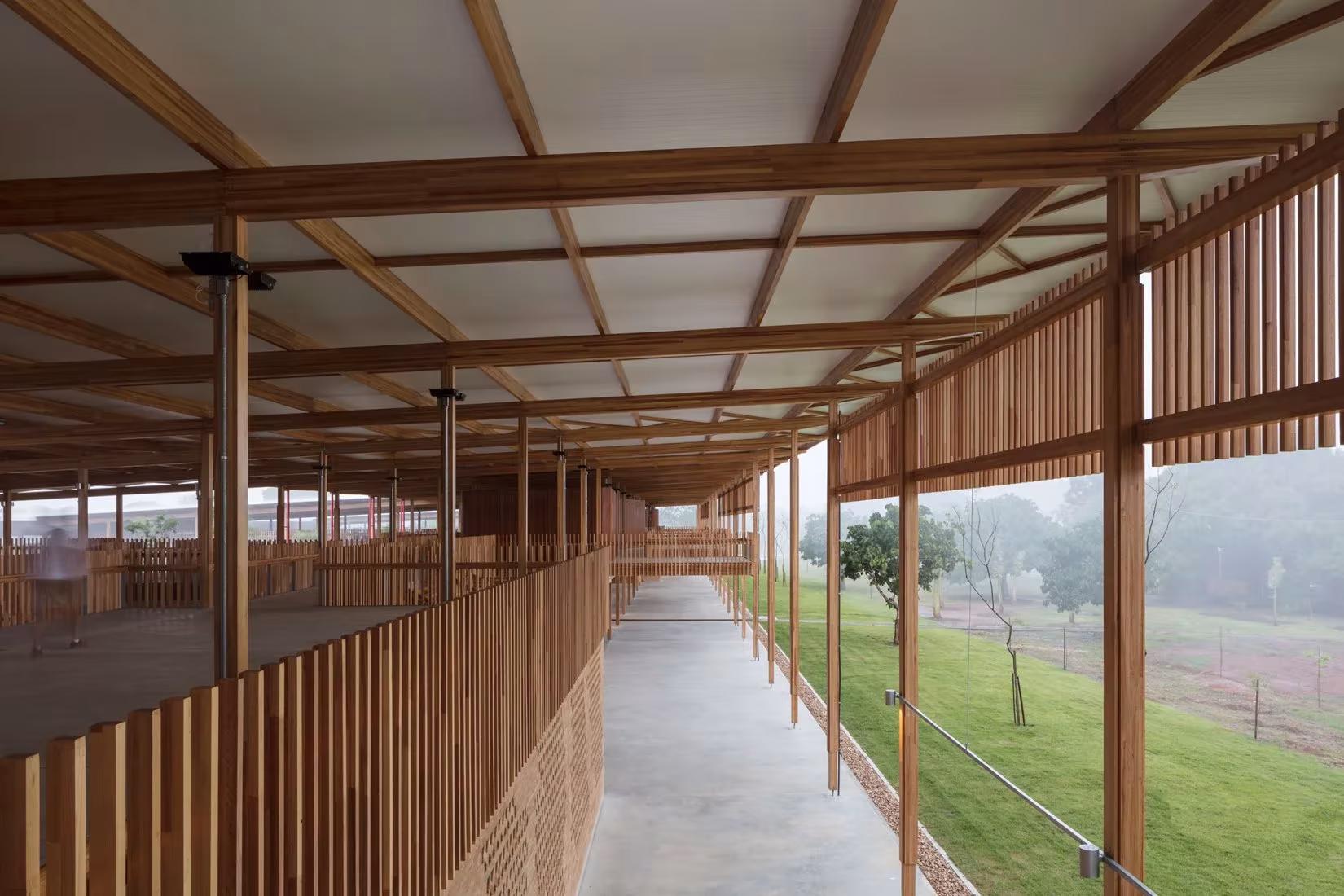 Galería de la Ciudad de los niños con barandilla de listones y estructura de madera abierta al campo