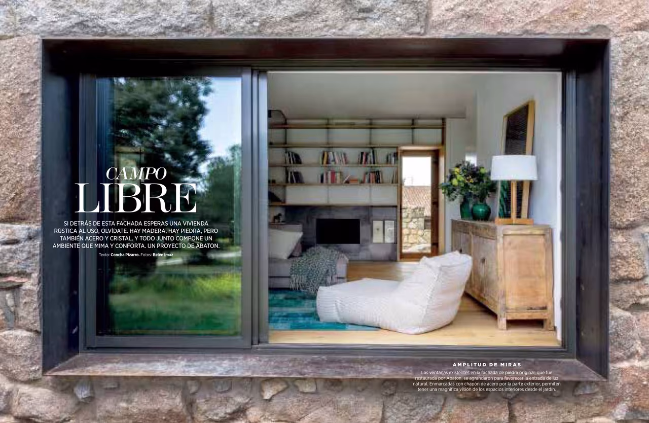 Ventana de piedra y marco oscuro con salón y librería al fondo en el reportaje Campo Libre de Nuevo Estilo