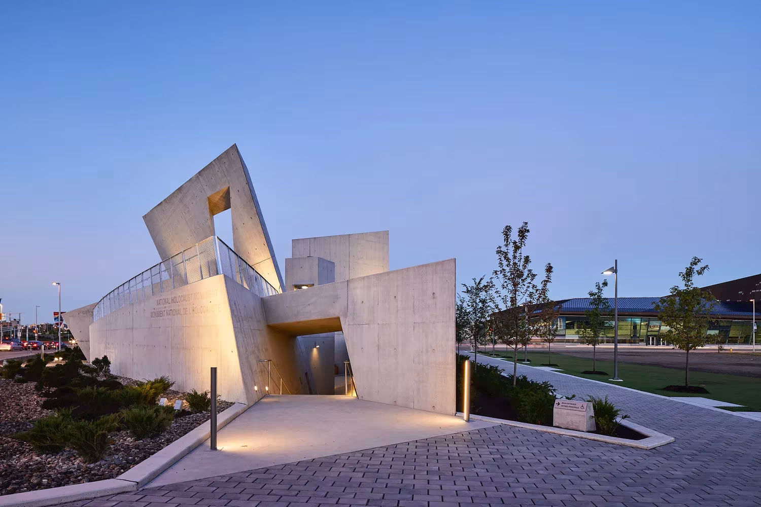 Acceso iluminado entre muros de hormigón del Monumento del Holocausto de Studio Libeskind al anochecer, en Ottawa