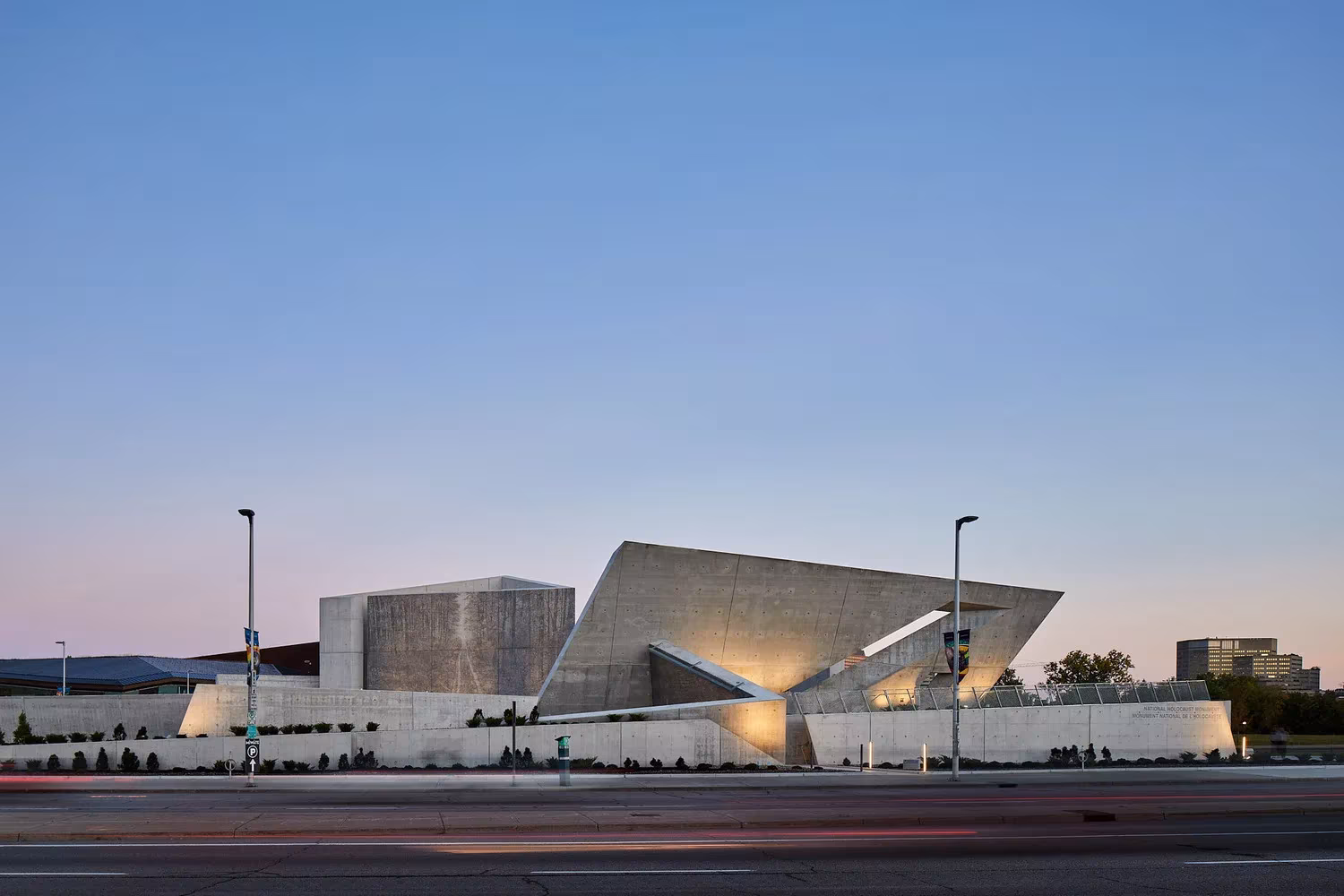 Volúmenes triangulares de hormigón del Monumento Nacional del Holocausto al atardecer, junto a una avenida de Ottawa