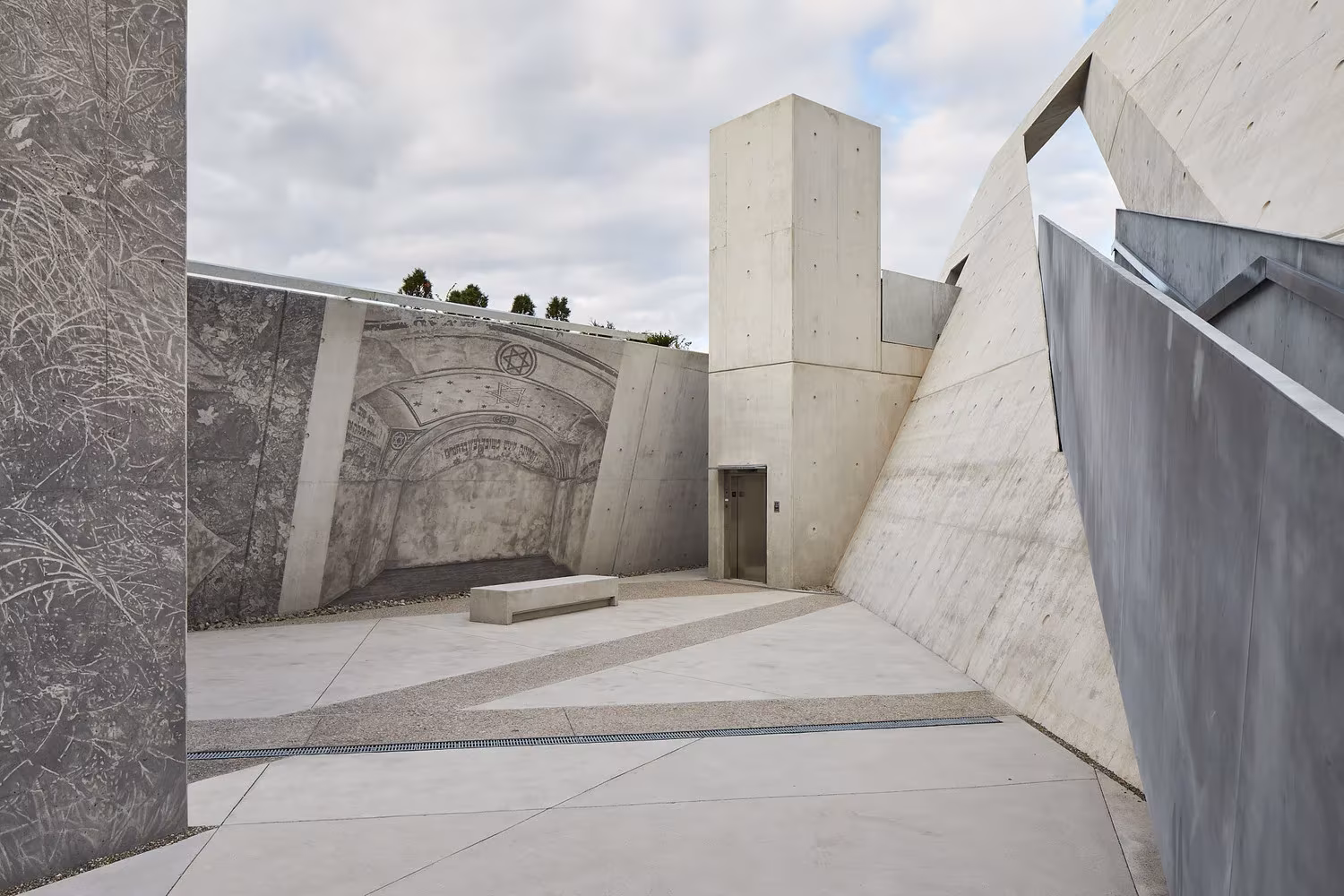 Patio del monumento con muro de piedra grabado y torre de hormigón, en el Monumento del Holocausto de Ottawa