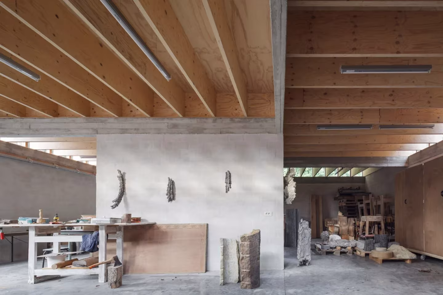 Interior del estudio con techo de vigas de madera y muro blanco central en la casa taller de Mariakerke