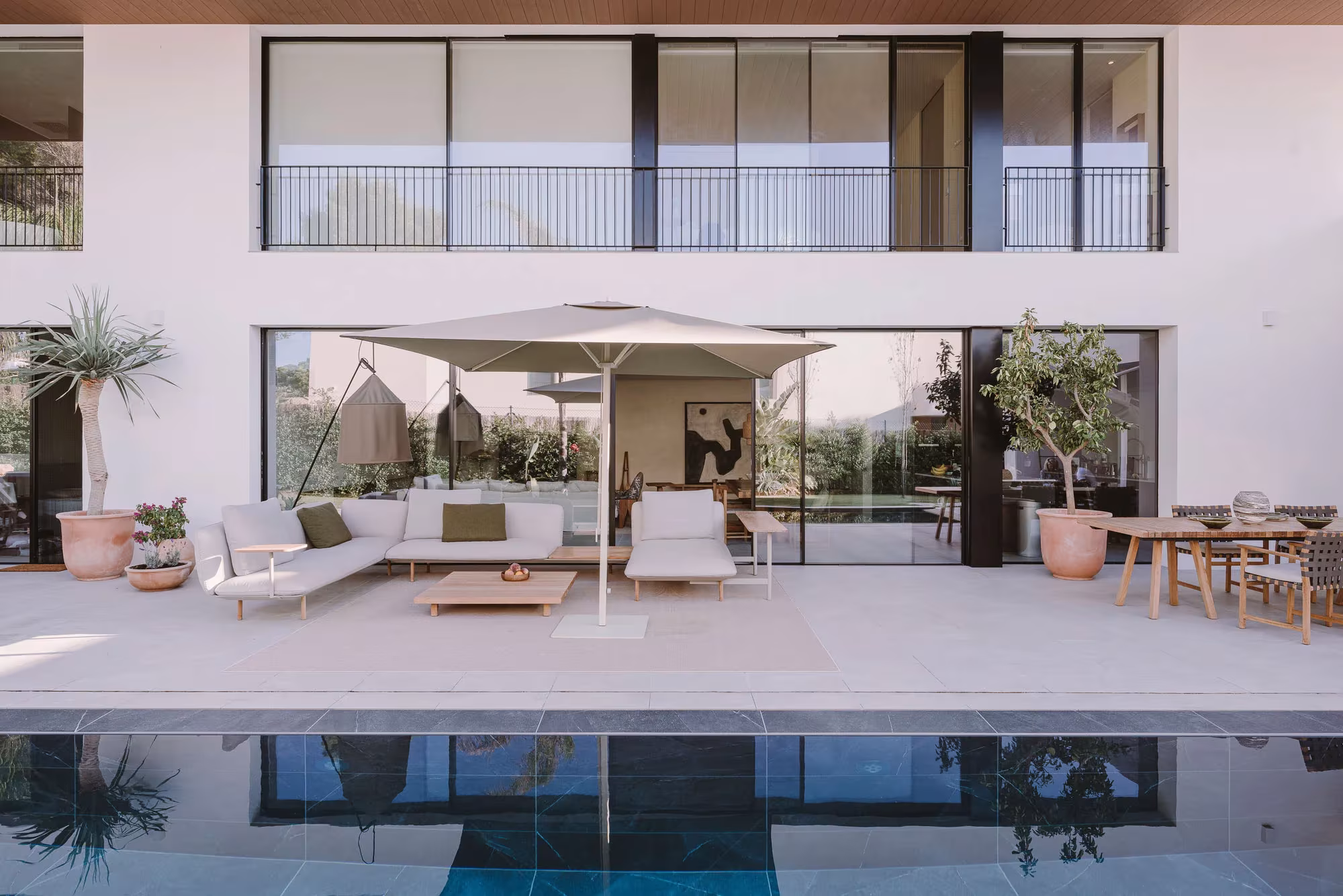 Terraza con sofás y sombrilla junto a la piscina ante la fachada blanca de la PDM House en Palma