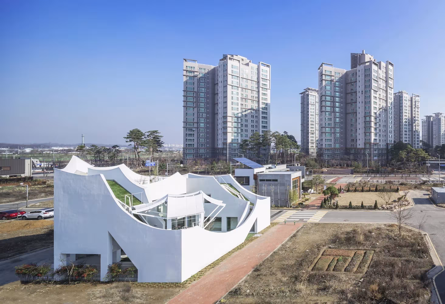Casa voladora de IROJE KHM Architects en Incheon, volumen blanco de curvas y rampas ante torres de viviendas