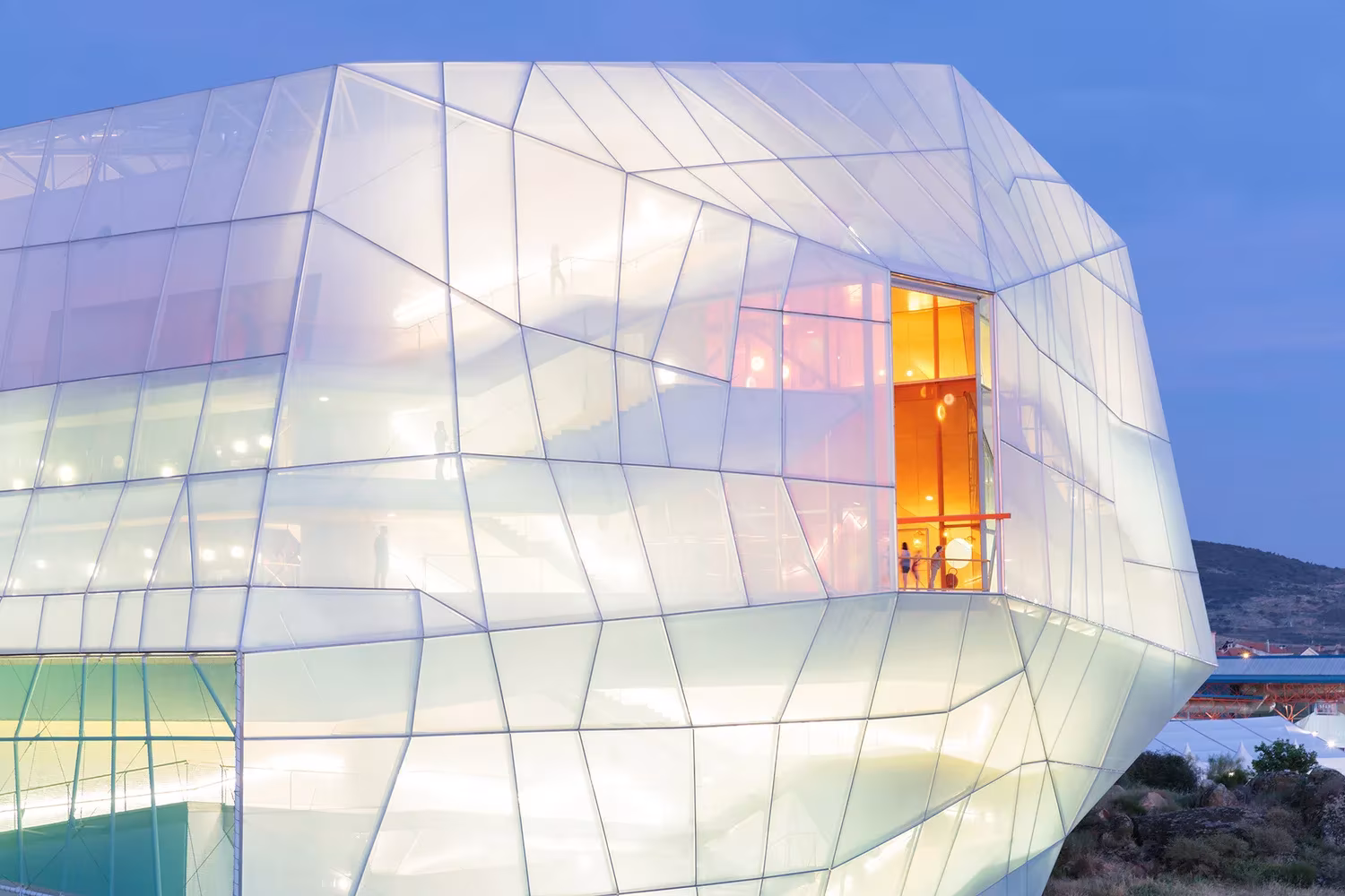 Palacio de Congresos de Plasencia de Selgas Cano iluminado al atardecer, con una ventana naranja en la piel blanca