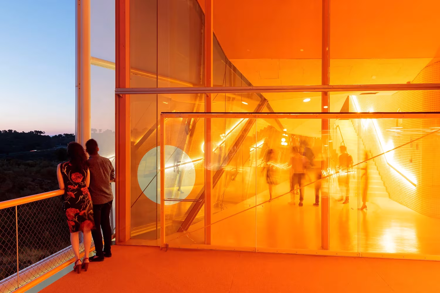 Pasillo naranja con muro de vidrio y pareja asomada al paisaje en el Palacio de Congresos de Plasencia, Selgas Cano