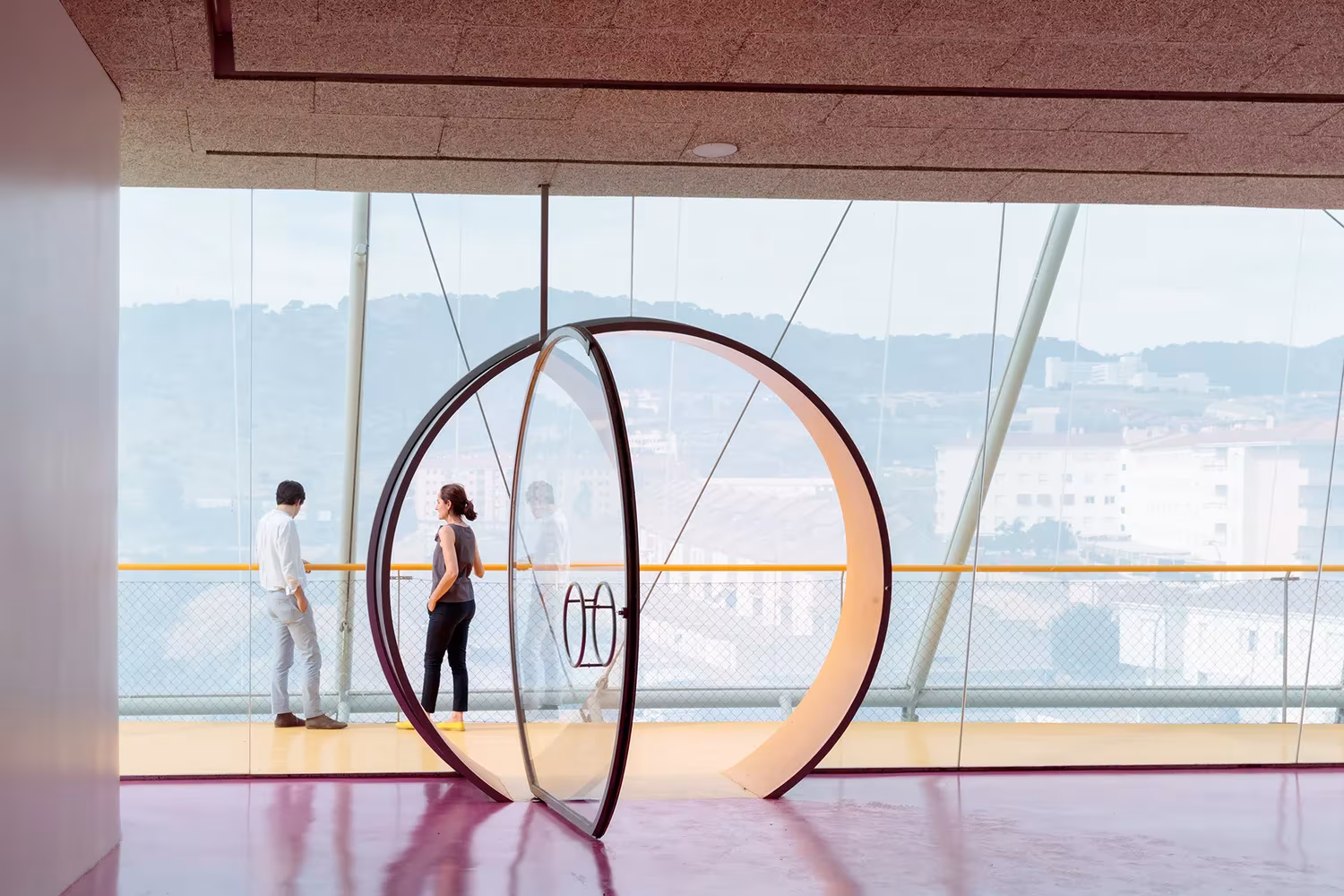 Visitantes ante un gran ventanal con puerta circular y vistas a la ciudad en el Palacio de Congresos de Plasencia