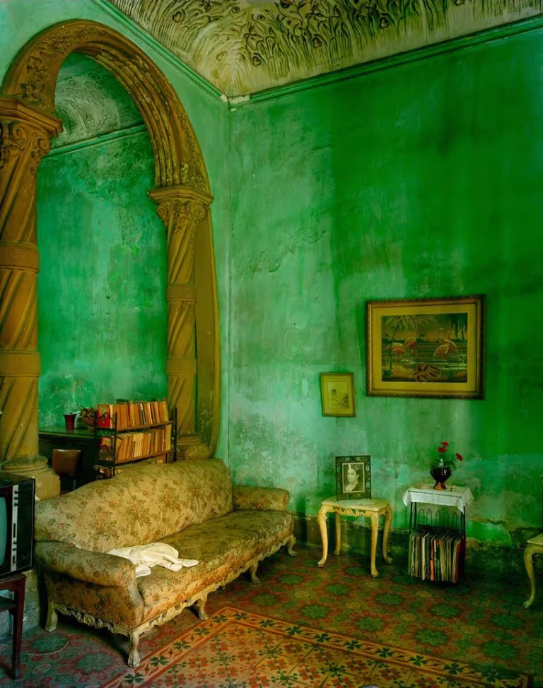 Salón colonial deteriorado de La Habana con paredes verdes desconchadas, sofá tapizado y arco ornamentado