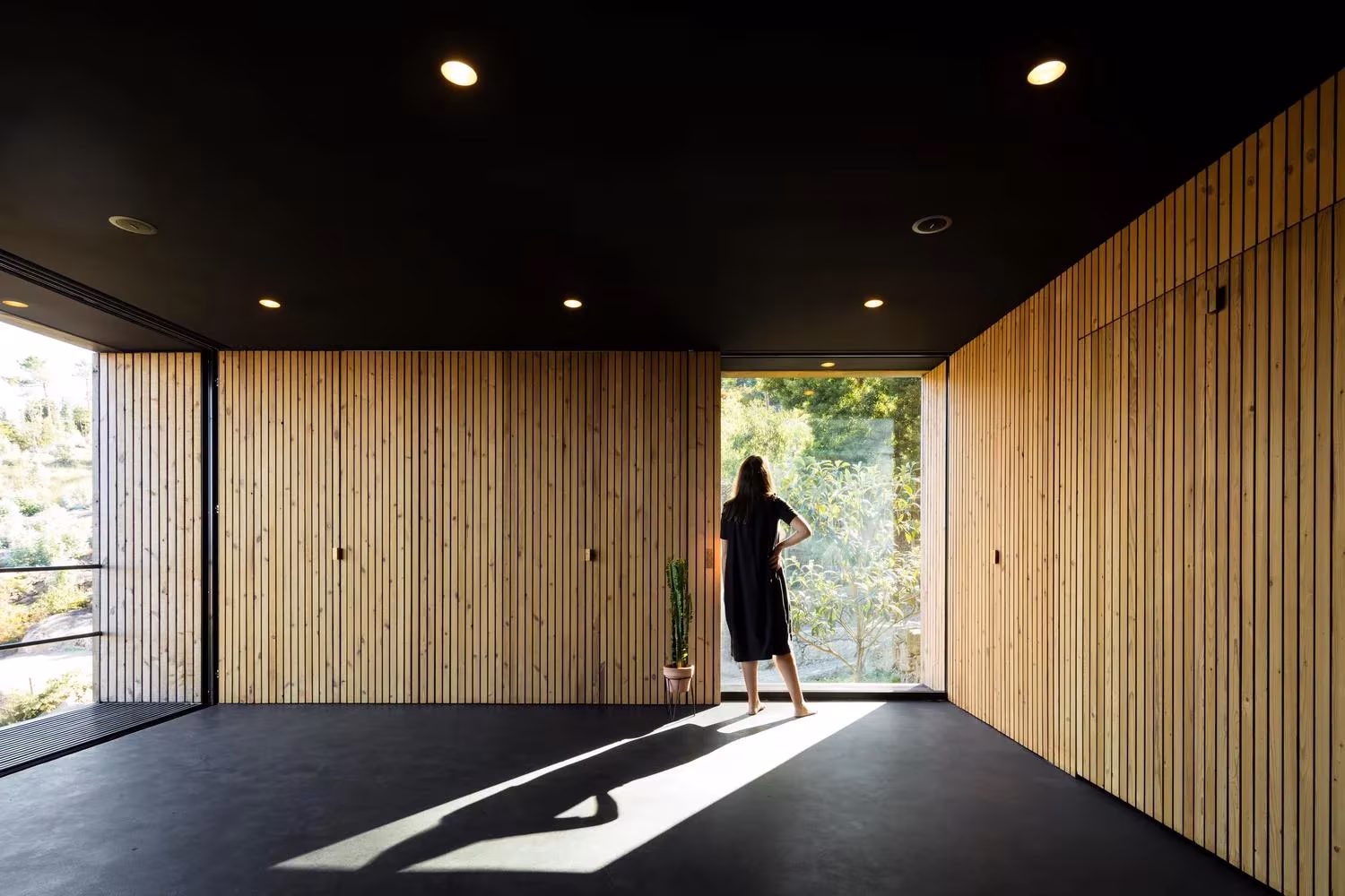 Estancia de paneles de madera y techo negro con una mujer ante un gran hueco, en la casa-pabellón de Guimarães