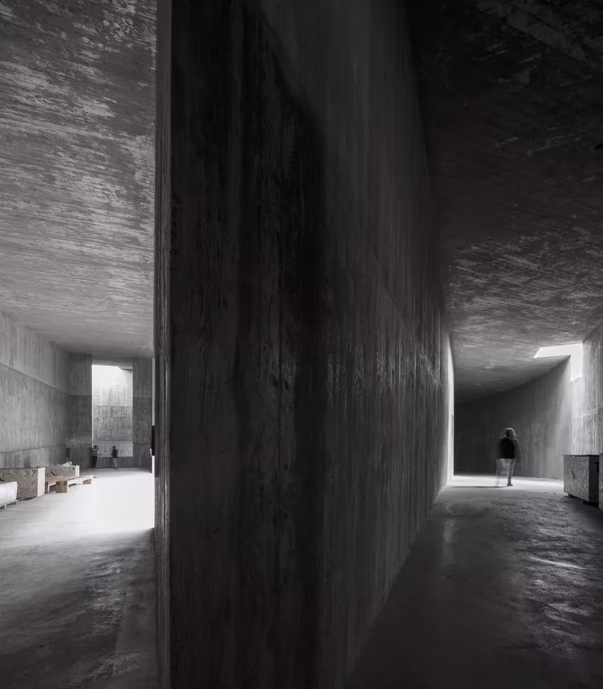 Corredor de hormigón en penumbra que se abre a una sala luminosa en el pabellón de Álvaro Siza en Saya Park