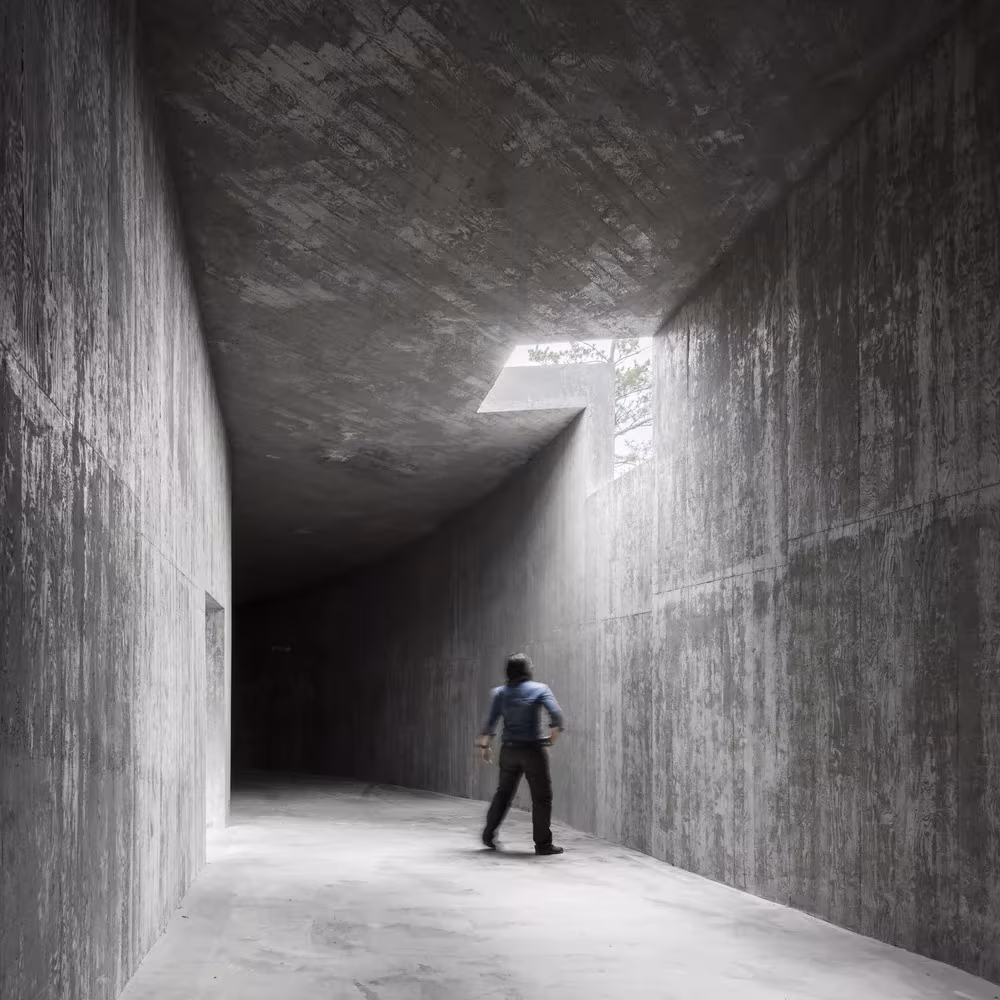 Persona en un corredor de hormigón con techo inclinado y una rendija de luz en el pabellón de Siza, Saya Park