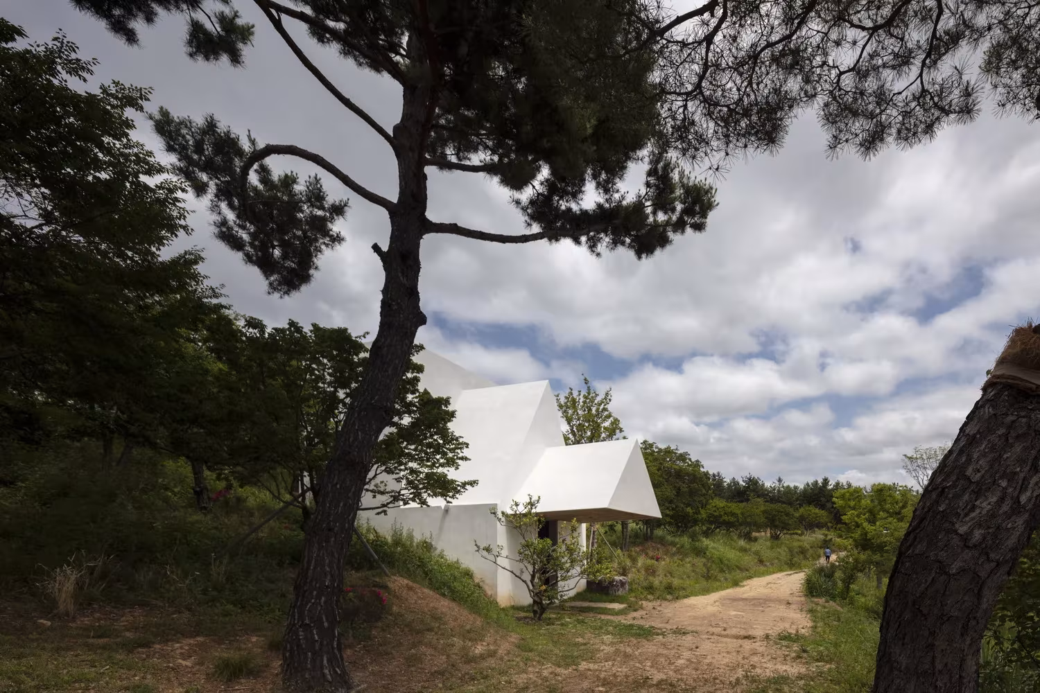 Pequeña casa blanca de cubiertas a dos aguas entre pinos y senderos de tierra en Saya Park, Corea del Sur