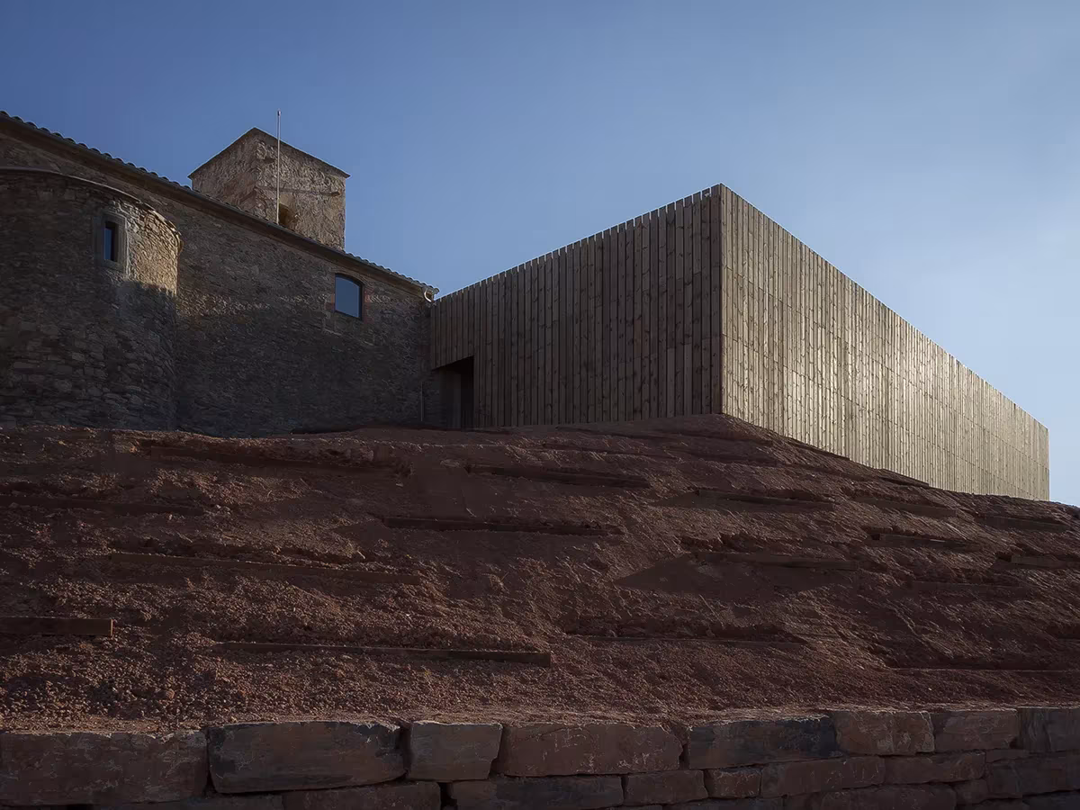 Nuevo volumen de listones de madera junto al muro de piedra de la iglesia de Sant Sadurní de Callús, de Puig-Mir