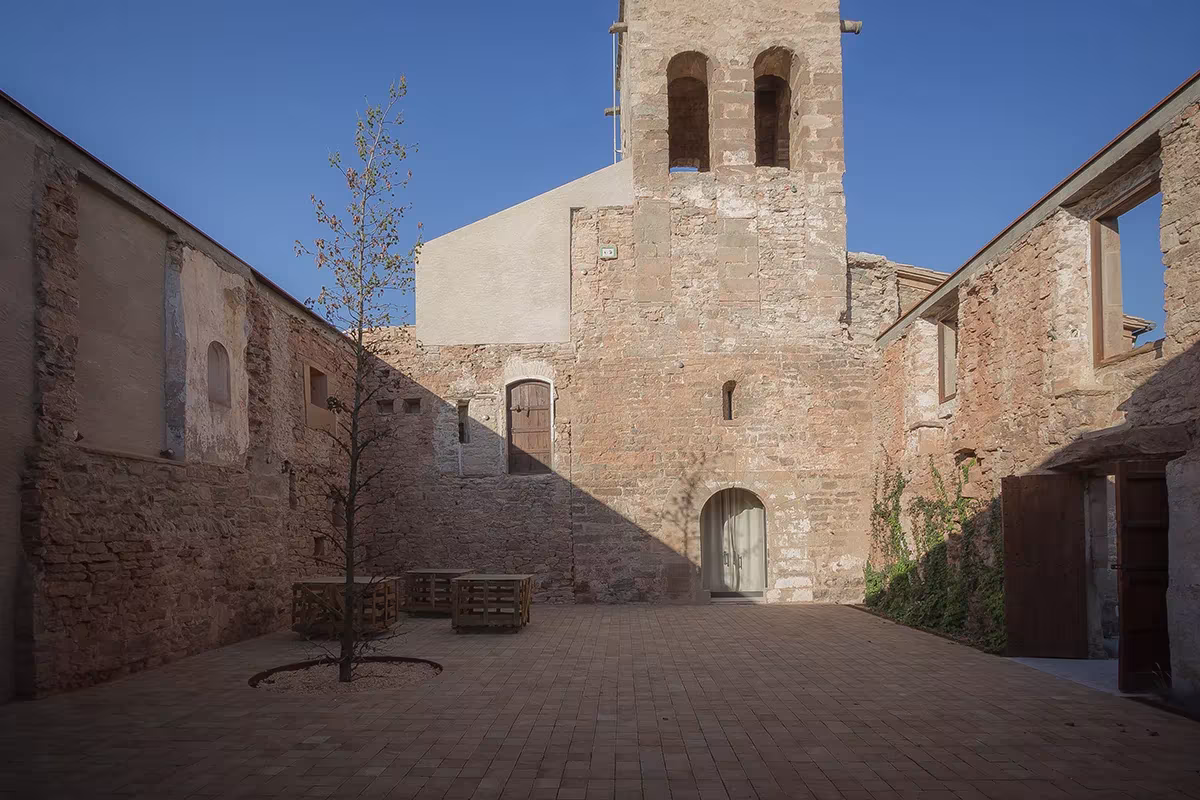 Patio de adoquín con un árbol y las ruinas de piedra de la iglesia de Sant Sadurní de Callús