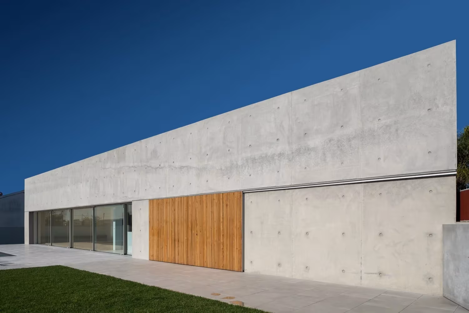 Fachada alargada de hormigón visto con panel de madera y ventanales en la Casa en Avanca de nu.ma