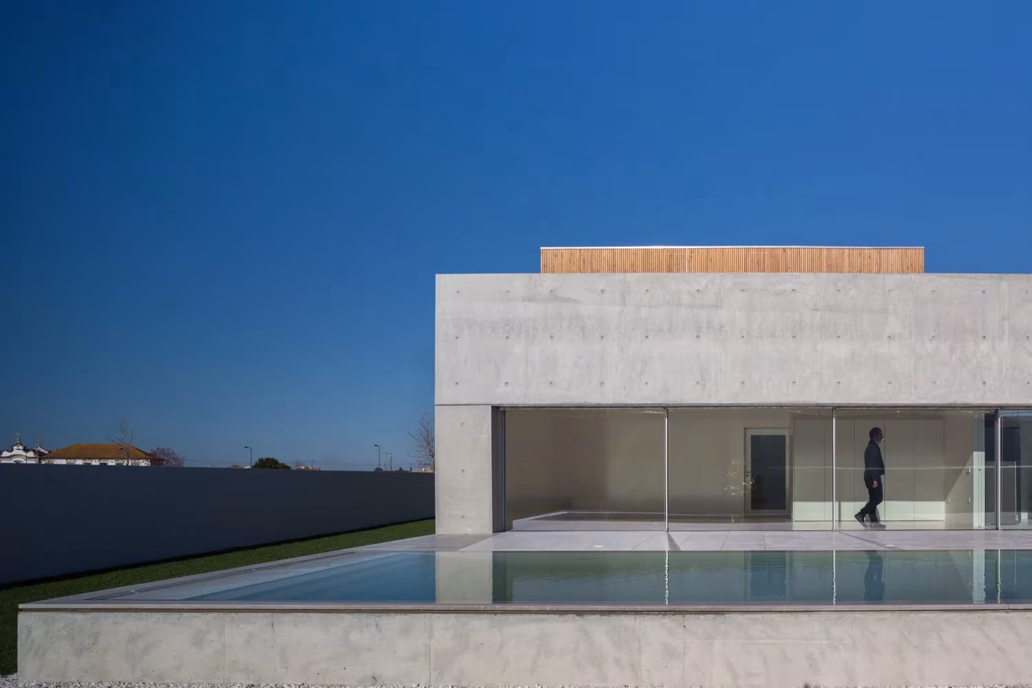 Salón acristalado de la Casa en Avanca abierto a la piscina bajo un volumen de hormigón visto