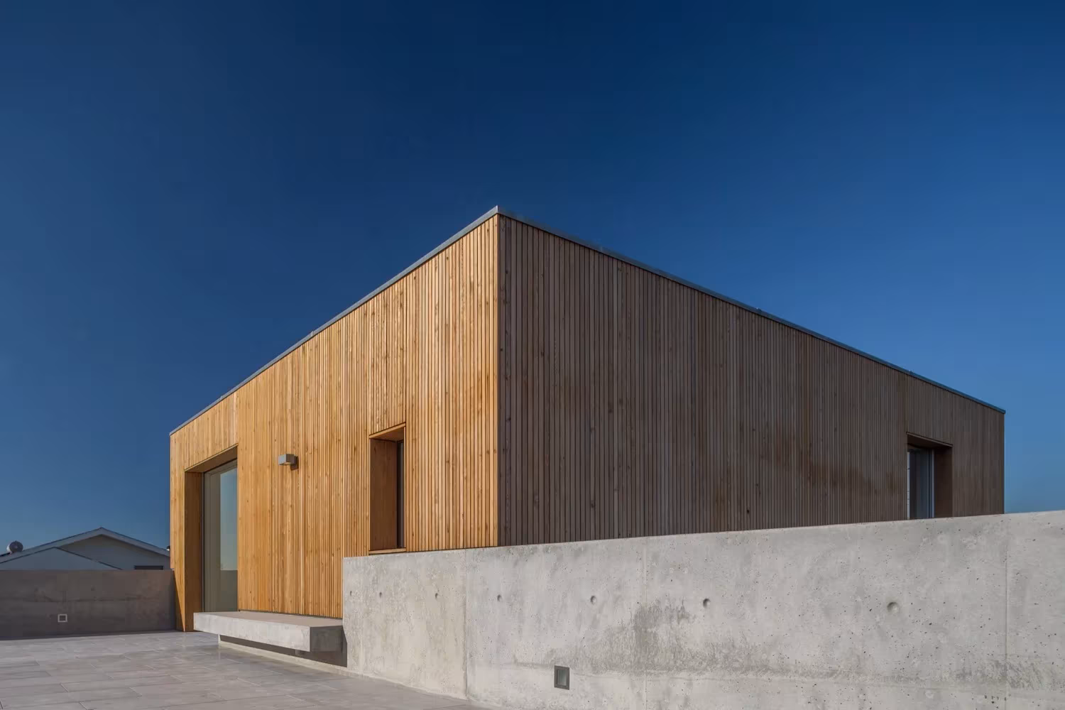 Casa en Avanca de Nuno Silva con fachada de lamas de madera y muro bajo de hormigón visto