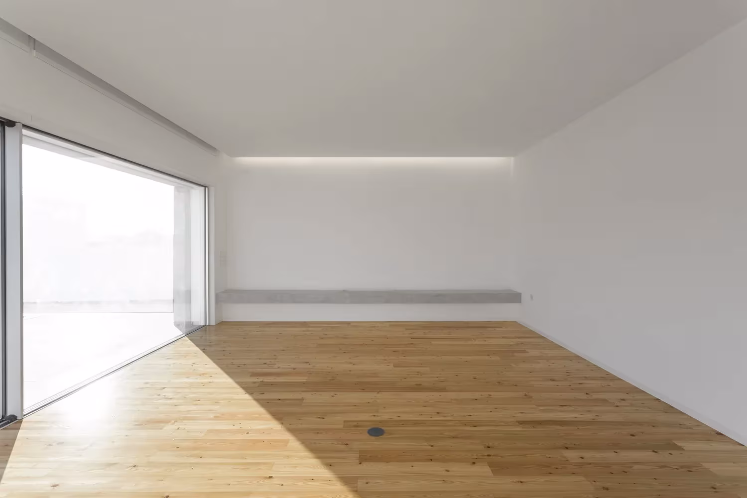 Sala vacía con suelo de madera, luz rasante y gran ventanal corredero en la Casa en Avanca de nu.ma