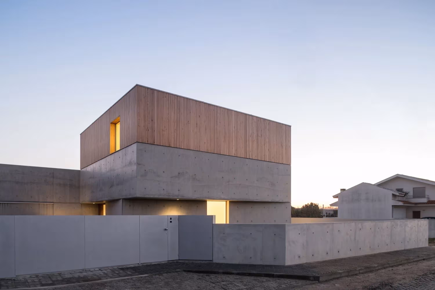 Casa en Avanca de Nuno Silva al anochecer, con el cubo de madera sobre el zócalo de hormigón y su muro