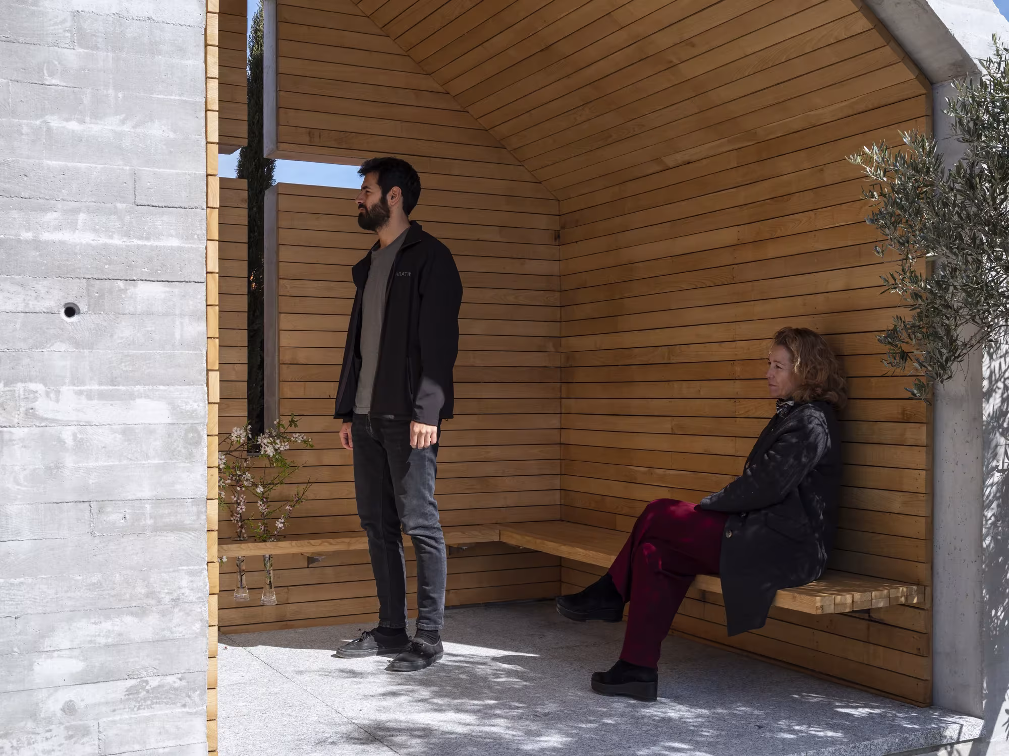 Interior del panteón con paredes de castaño, banco de madera y una cruz calada que deja pasar la luz