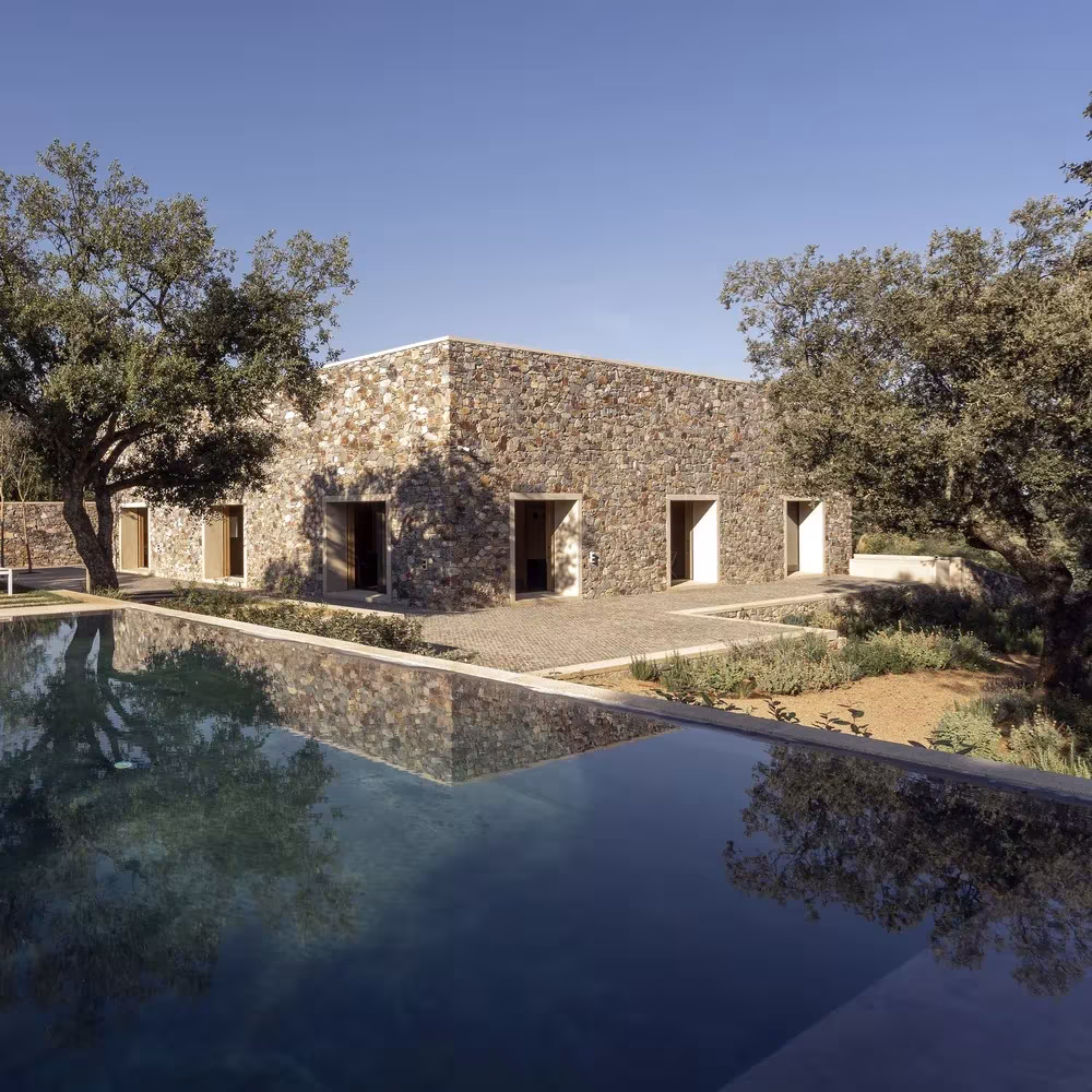 Piscina oscura junto a la Casa de piedra de Tuñón Arquitectos, con sus muros de mampostería y encinas