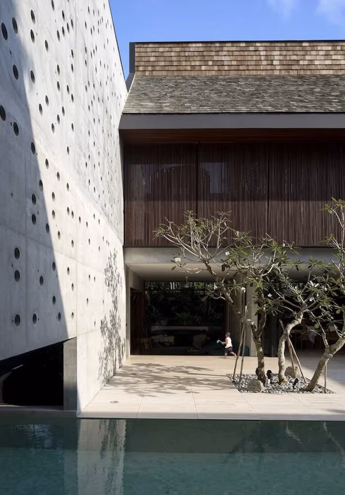 Muro de hormigón perforado con círculos y árbol en el patio de la Courtyard House de Singapur