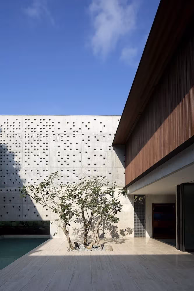 Patio de la Courtyard House con muro de hormigón calado y un árbol junto al agua, en Singapur