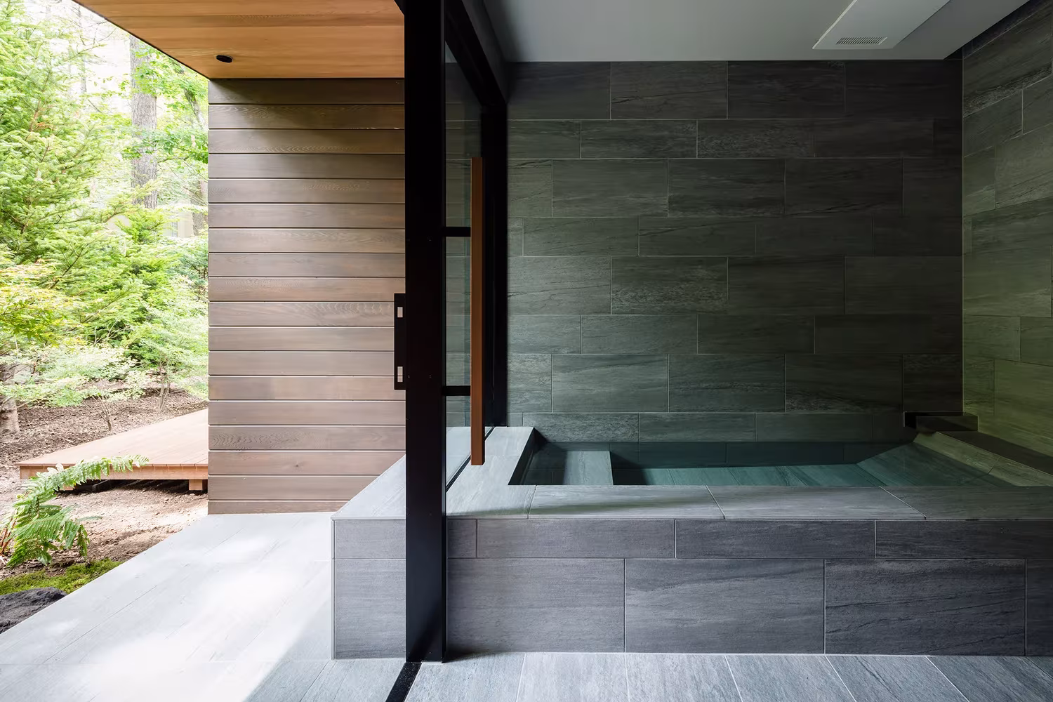 Baño de piedra con bañera junto a un muro de madera abierto al bosque en la Casa en Karuizawa de KIAS