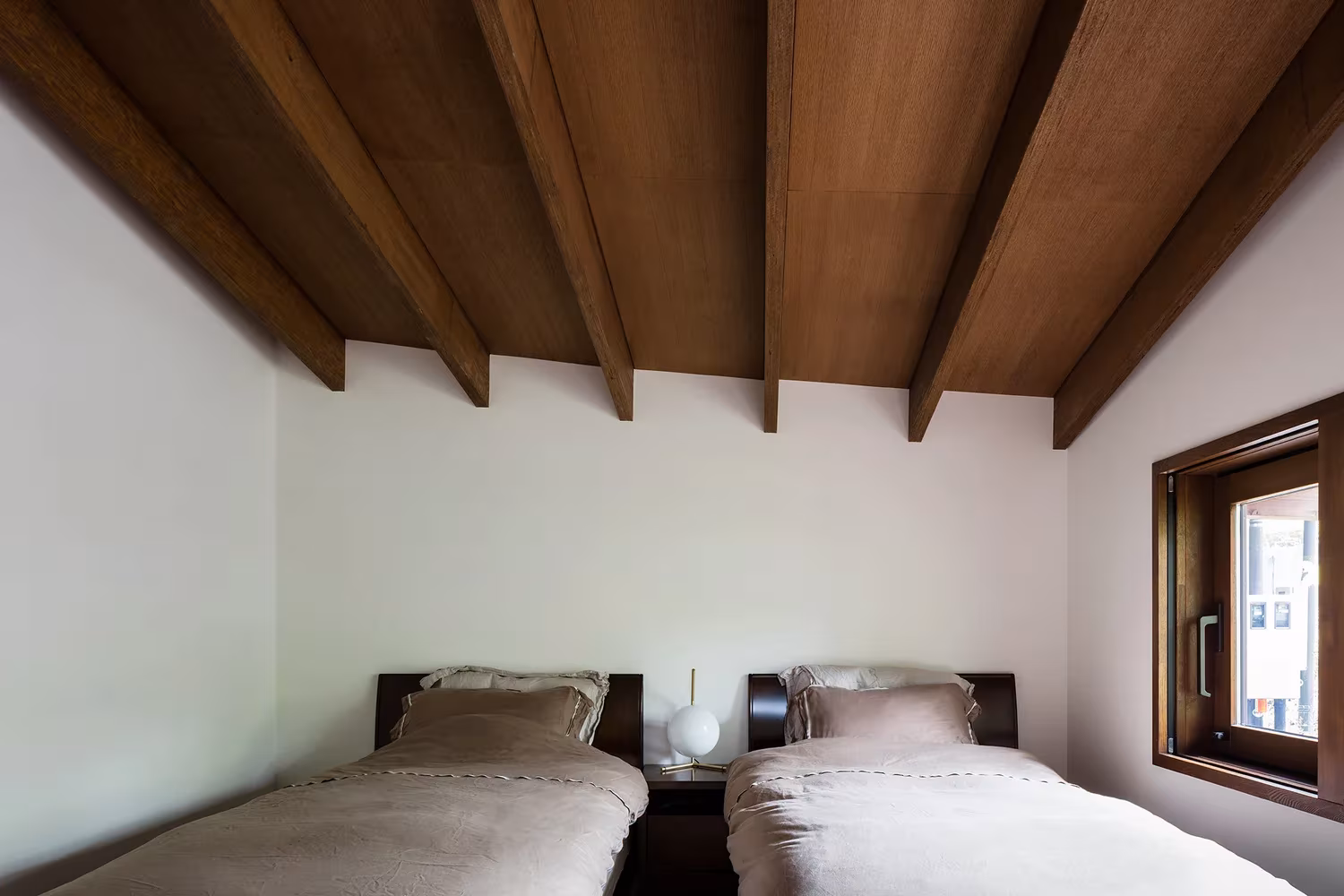 Dormitorio con camas gemelas y cubierta de vigas de madera inclinadas en la Casa en Karuizawa