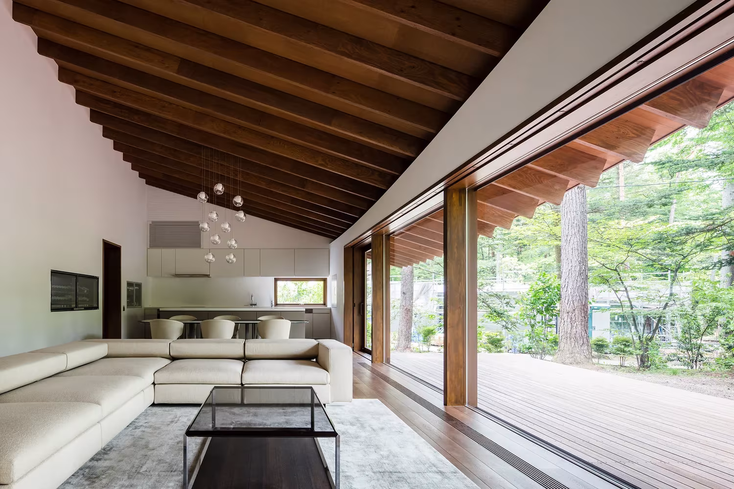 Salón de la Casa en Karuizawa con sofá blanco, techo de madera a dos aguas y corredera abierta al porche