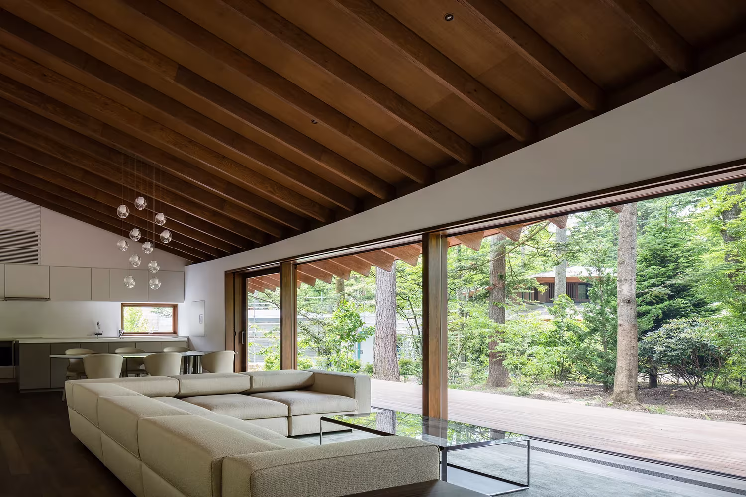 Sala de estar y comedor bajo la cubierta de vigas de madera de la Casa en Karuizawa de KIAS