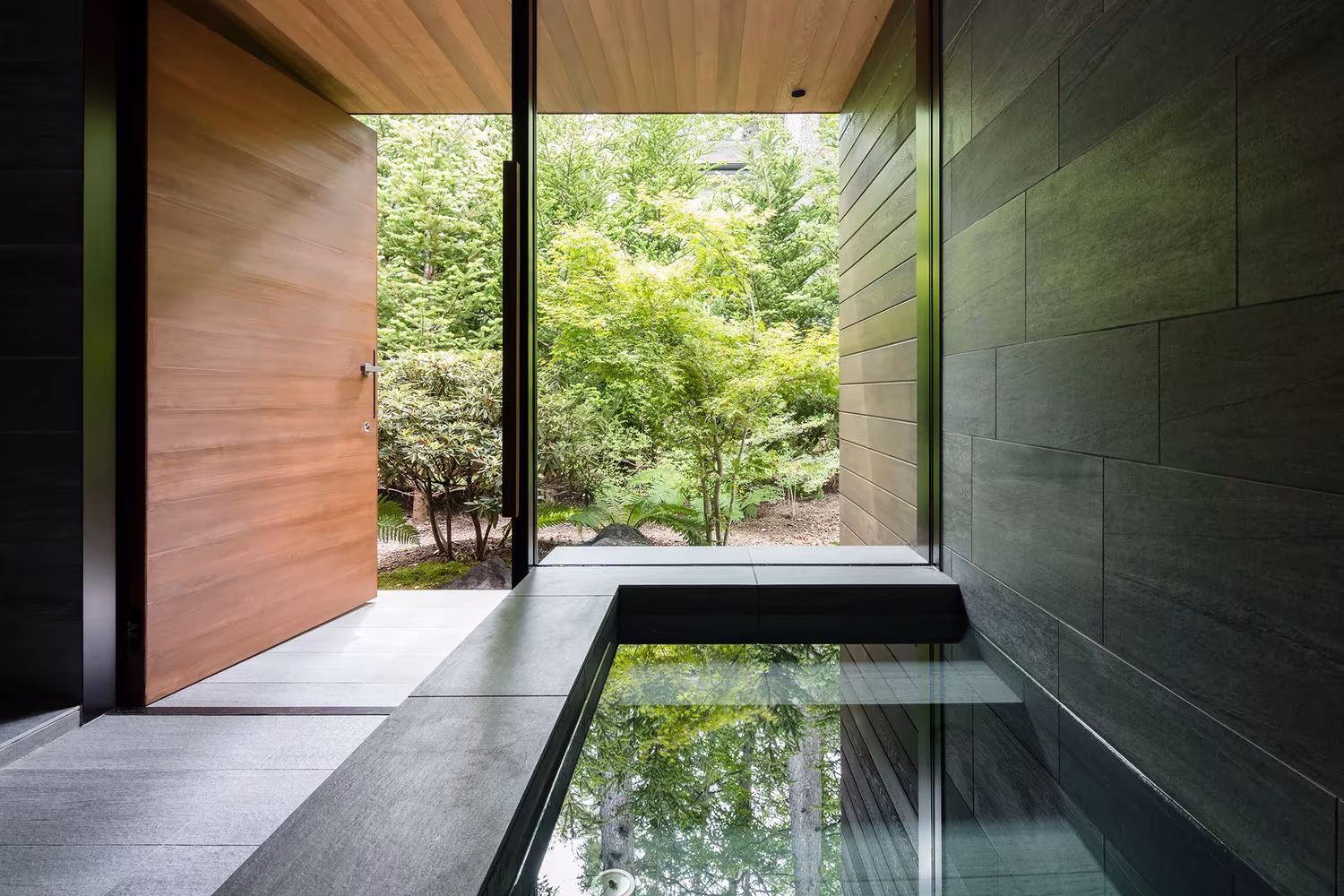 Pequeño estanque interior de vidrio y gran puerta pivotante de madera en la Casa en Karuizawa