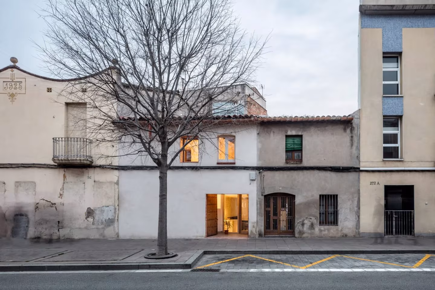 Fachada a la calle de la casa entre medianeras de DataAE en Sant Feliu de Llobregat, con la puerta iluminada
