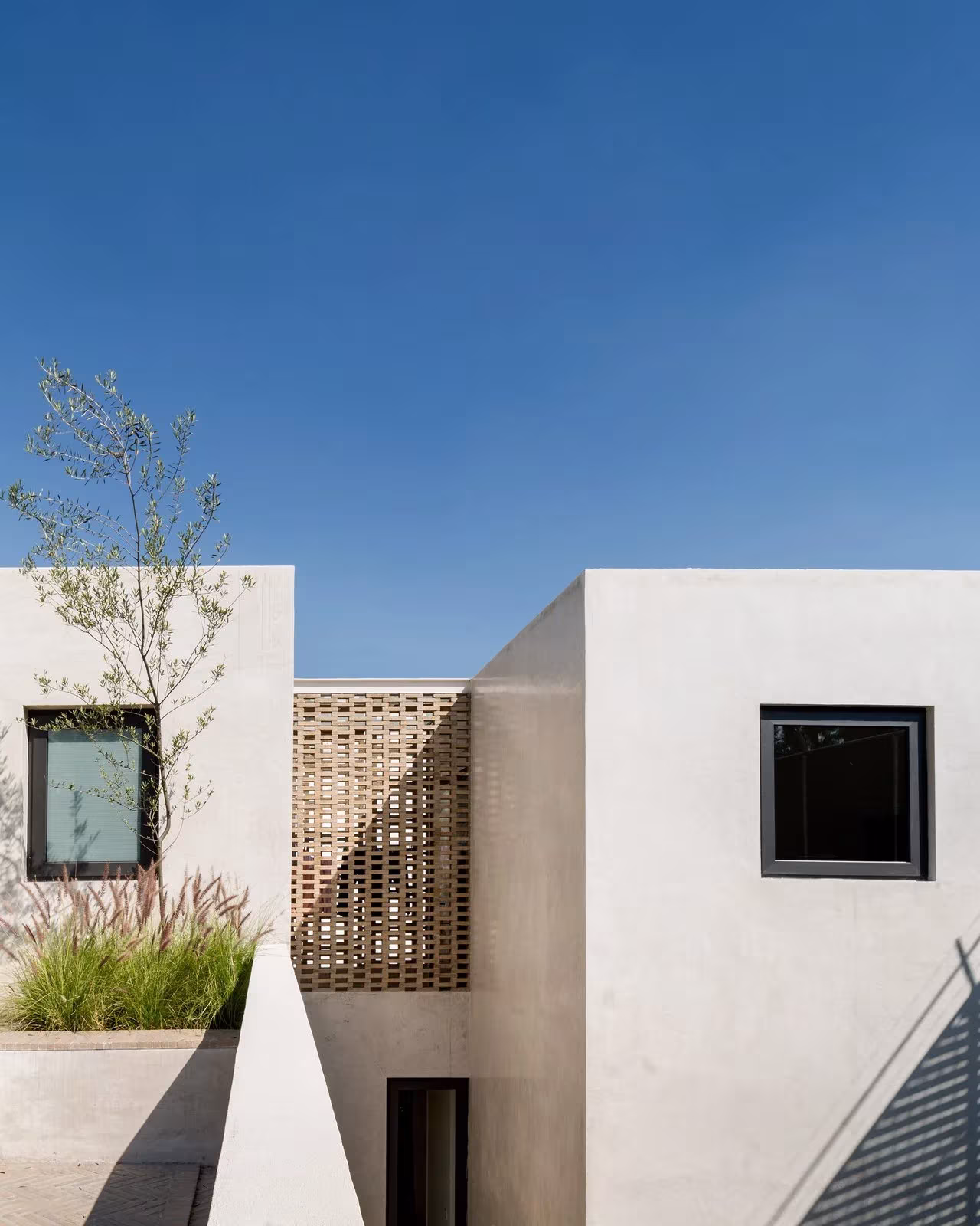 Volúmenes blancos de la Casa Jardín 58 con celosía cerámica y ventanas cuadradas sobre una azotea ajardinada
