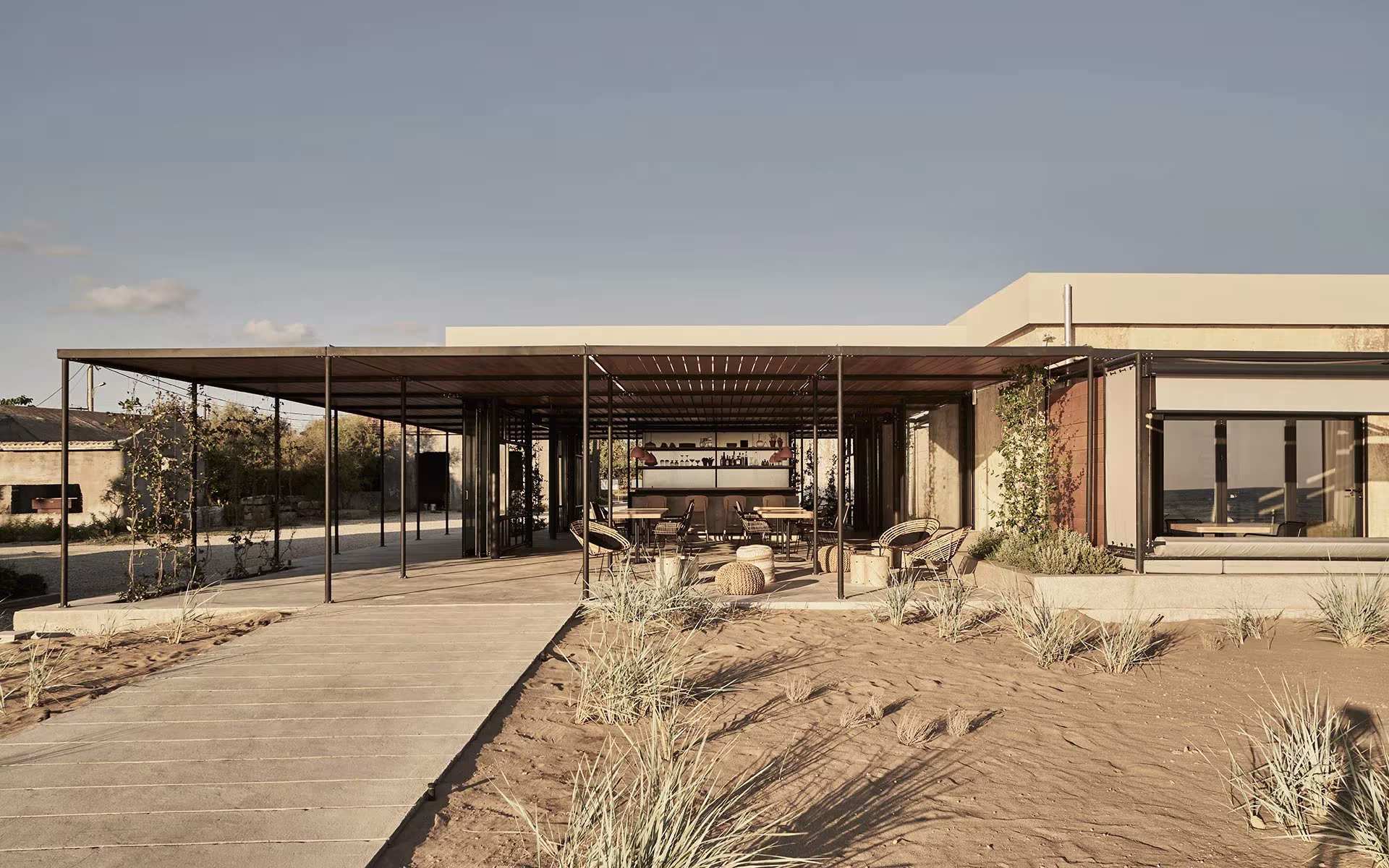 Pasarela de madera sobre la arena hacia los pabellones con pérgola del Dexamenes Seaside Hotel