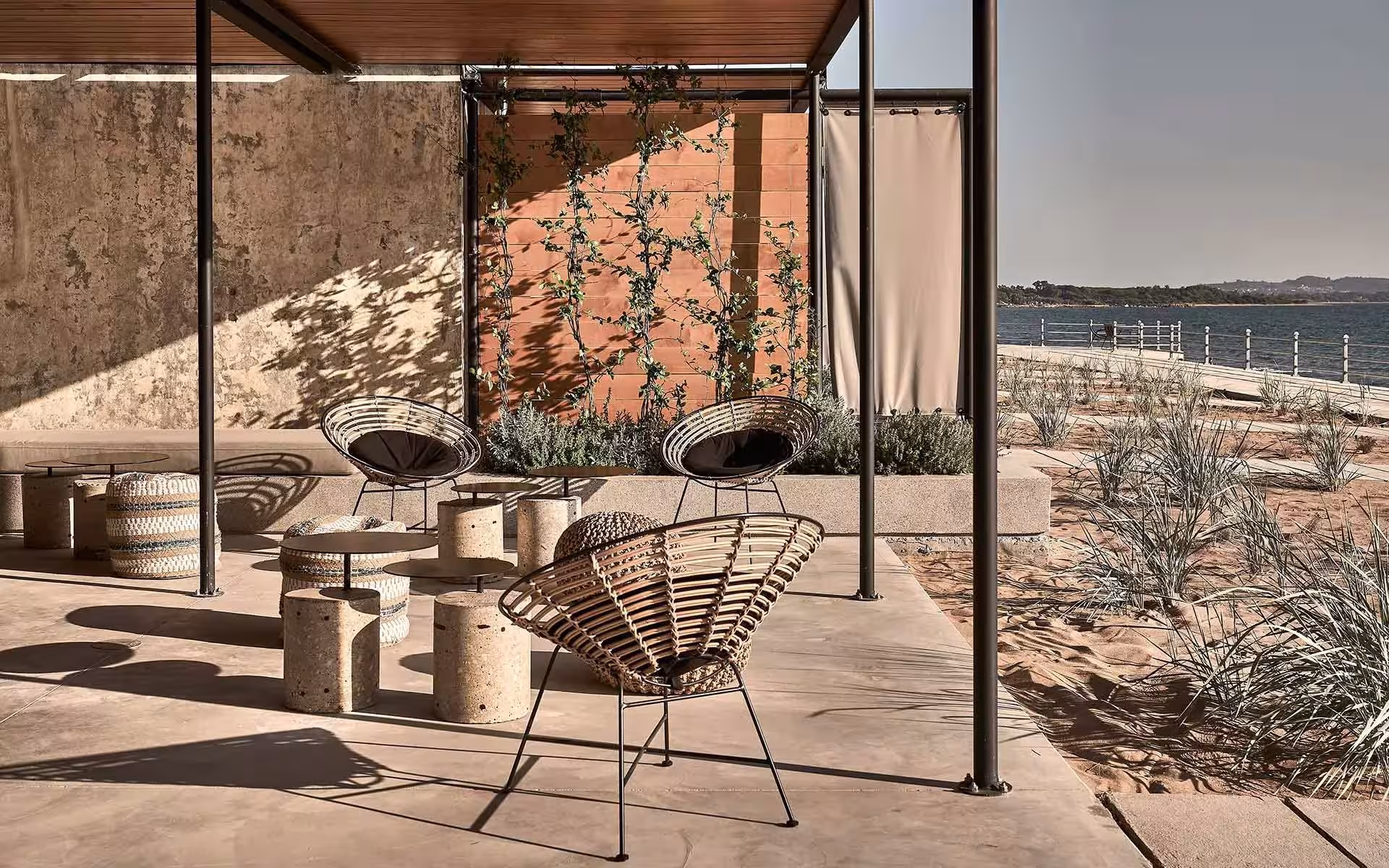 Terraza con pérgola metálica, sillones de rejilla y vegetación frente al mar en el Dexamenes Seaside Hotel