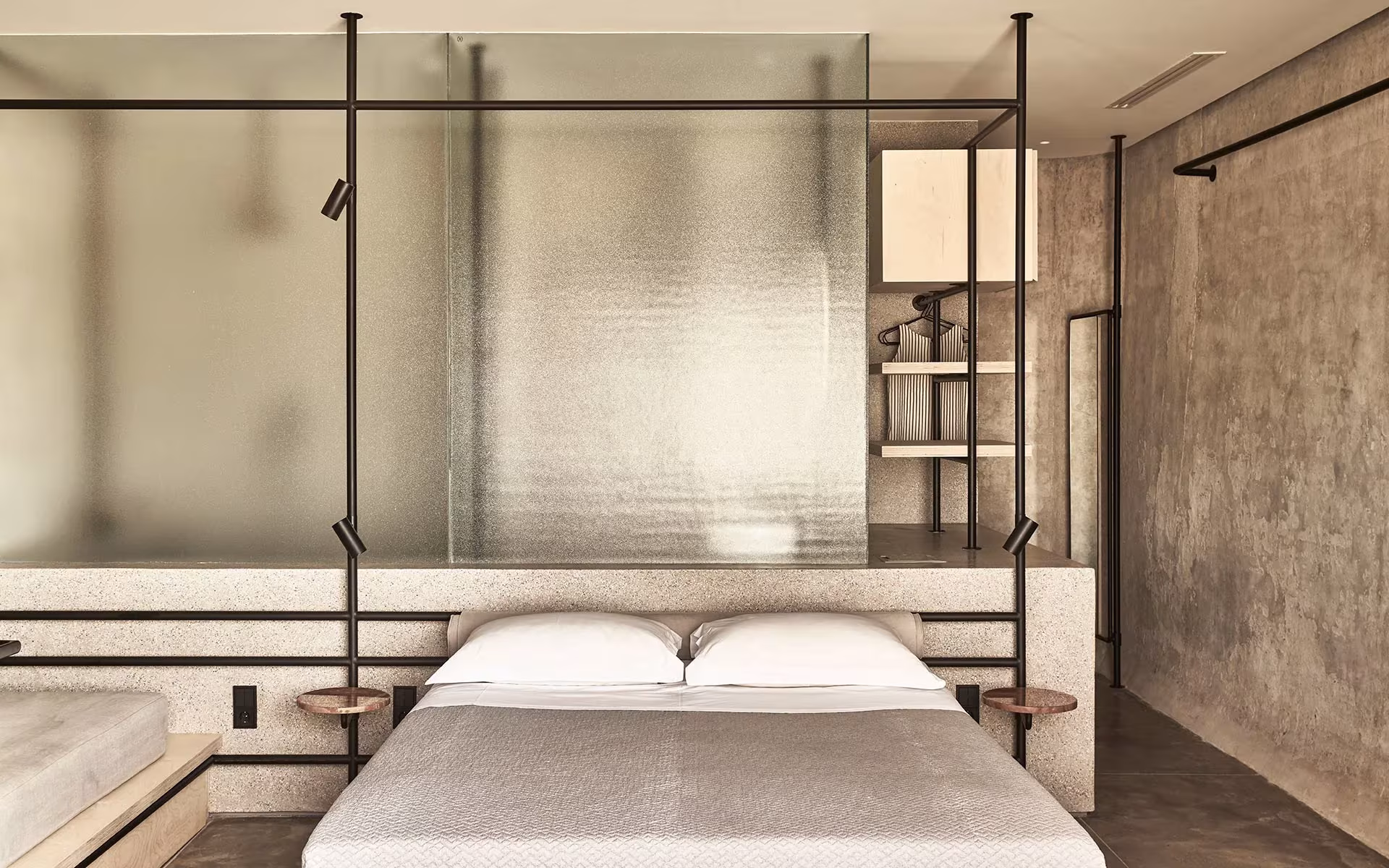 Dormitorio con mampara de vidrio translúcido, estructura de acero negro y muro de hormigón en el Dexamenes Seaside Hotel