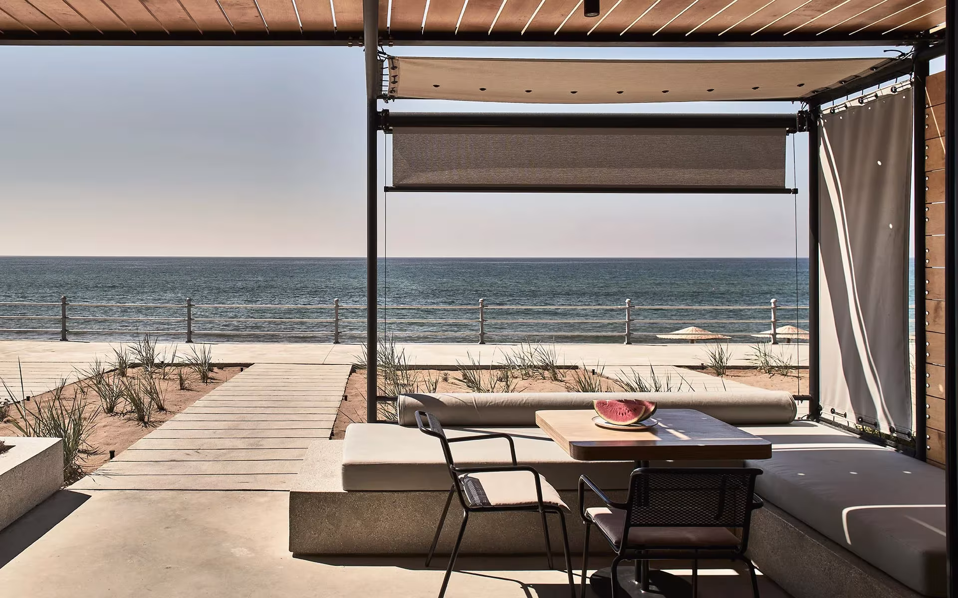 Pérgola con toldo y banco corrido de hormigón frente al mar en el Dexamenes Seaside Hotel, Peloponeso