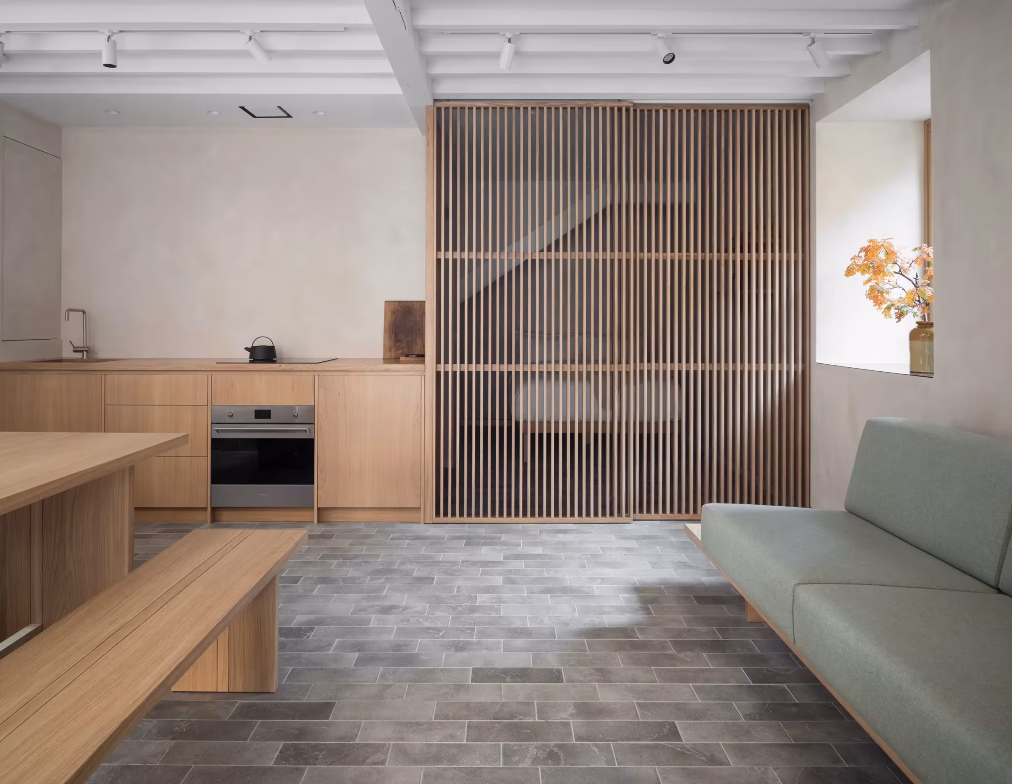 Cocina y salón del Porteous Studio con mueble de roble, banco y celosía de madera sobre suelo de baldosa