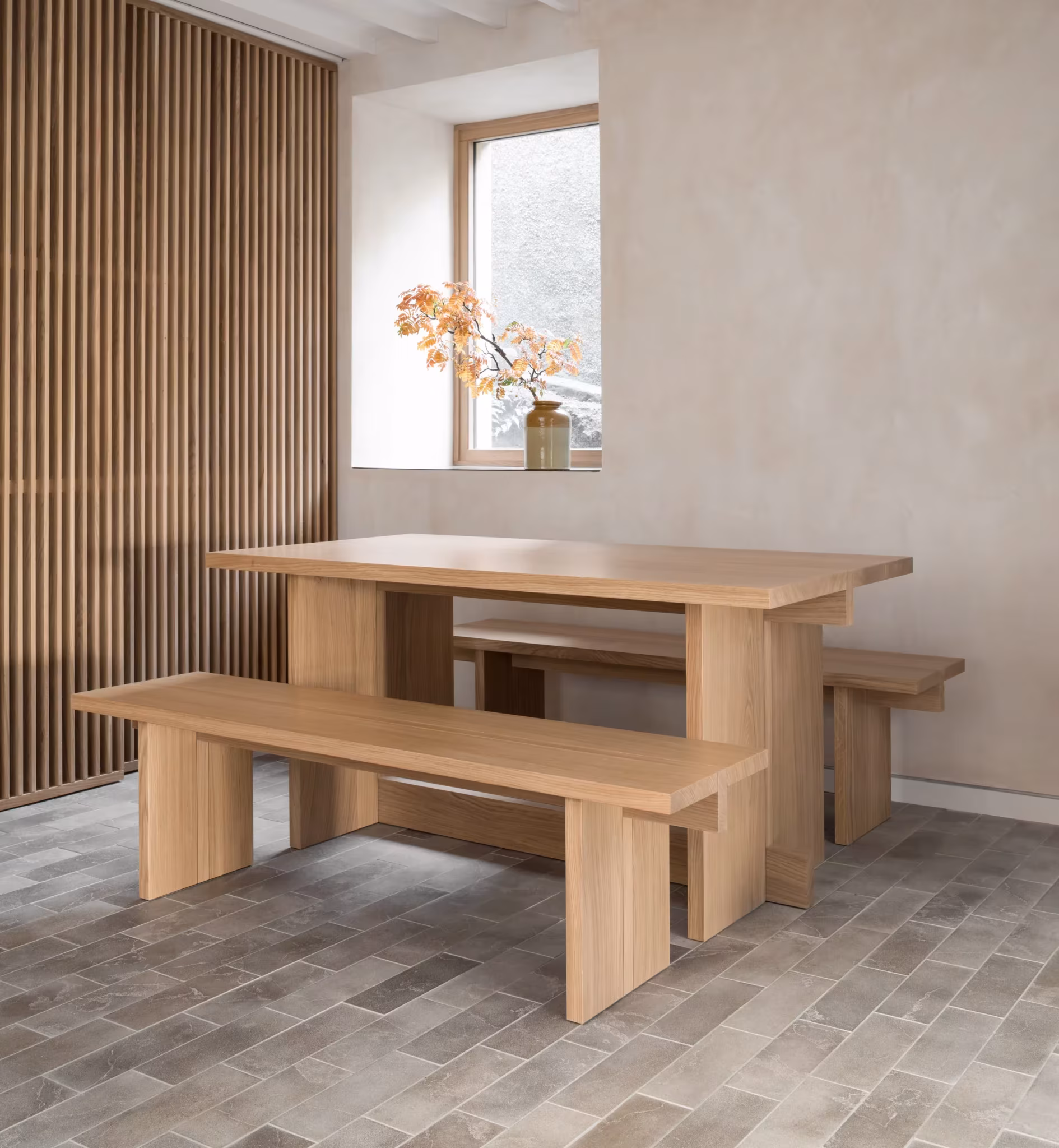 Comedor con mesa y bancos de roble, celosía de madera y ventana a la calle en el Porteous Studio