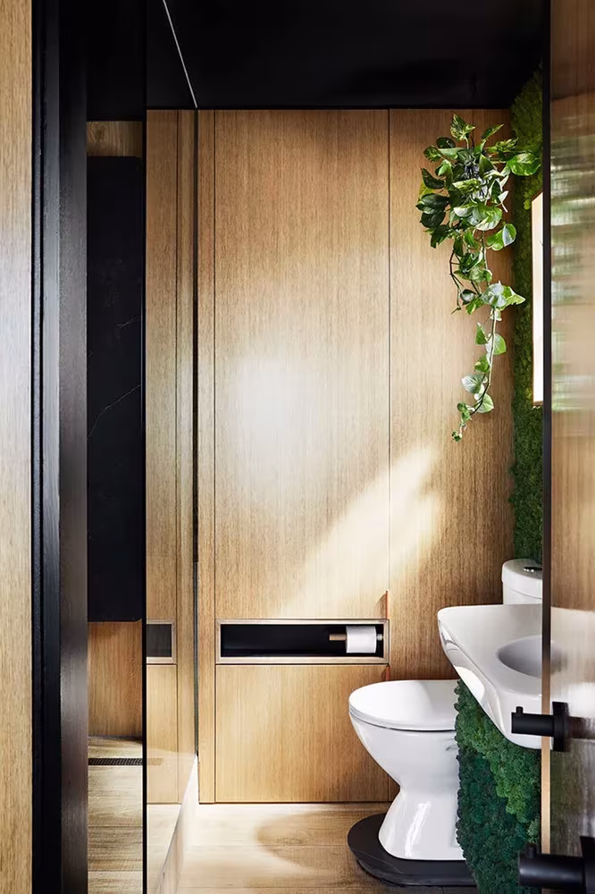 Baño con puerta de roble, pared vegetal y plantas trepadoras en el apartamento de Jack Chen, Melbourne
